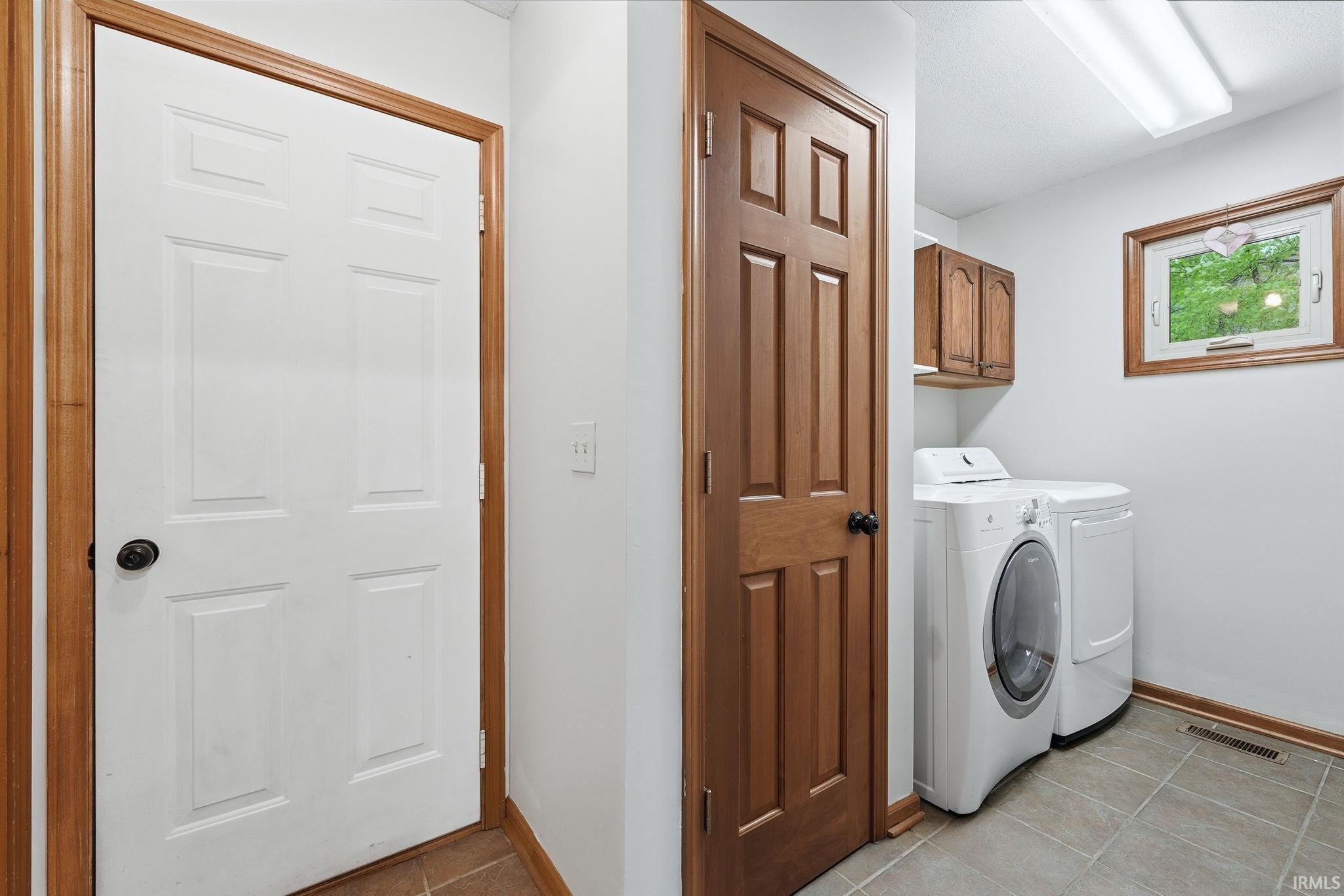 Dedicated laundry area featuring tile flooring, wood-finish cabinetry, and a framed window