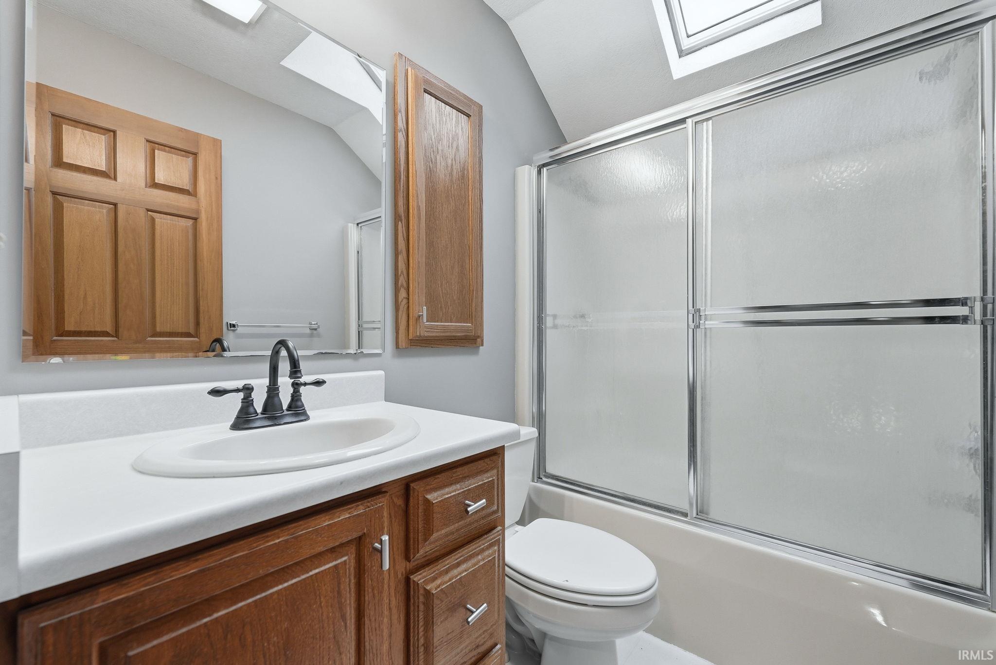 Bathroom featuring a vanity with a white countertop and wood-finish cabinetry, a black faucet, and a shower-tub combination with sliding glass doors