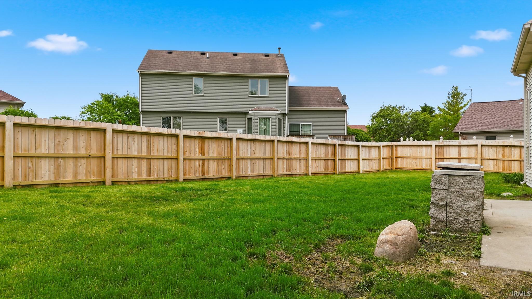 Expansive backyard featuring a lush green lawn, full wood privacy fencing, and a concrete patio section