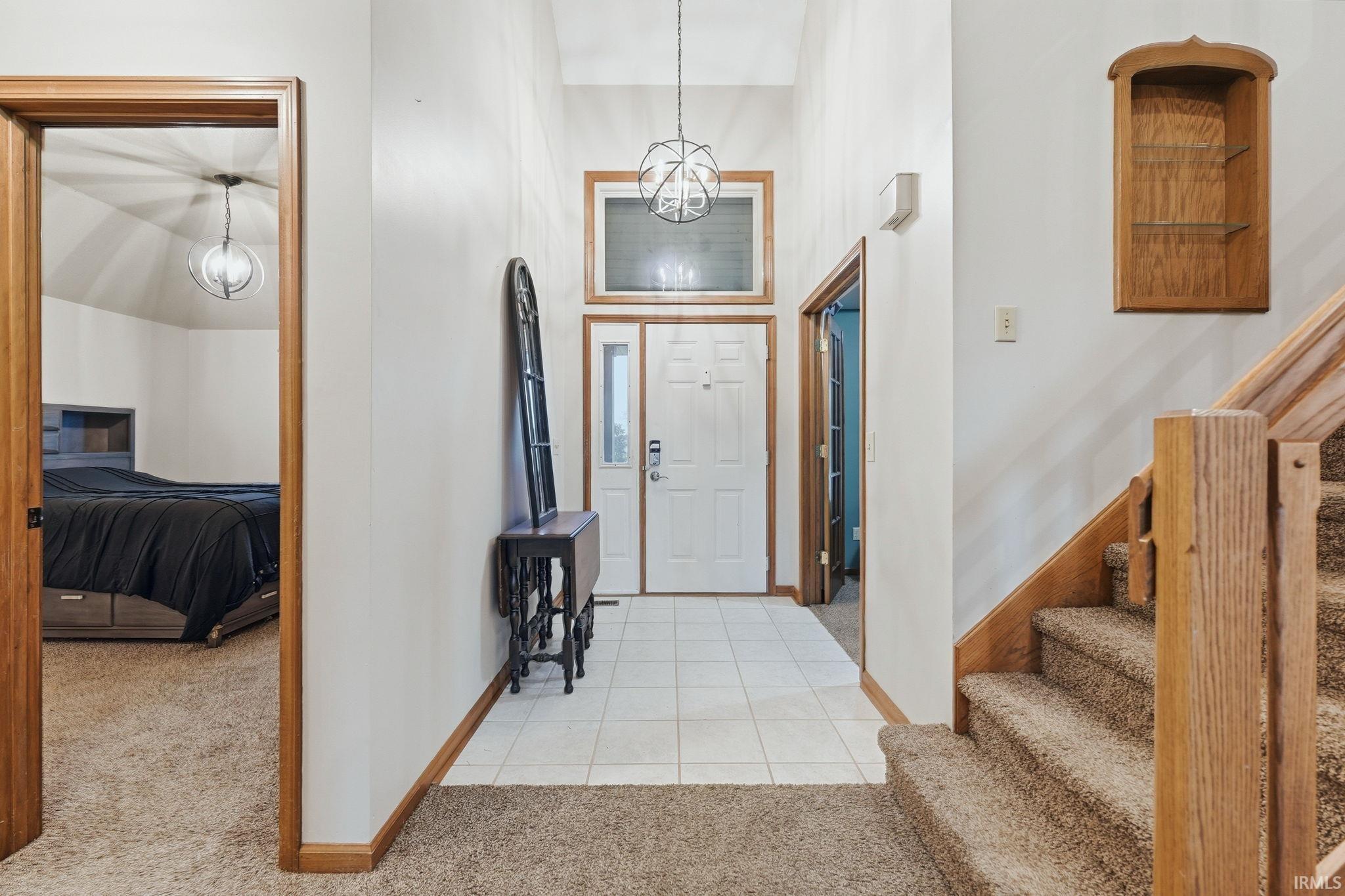Inviting entryway featuring a white paneled front door, overhead transom window, and a contemporary chandelier