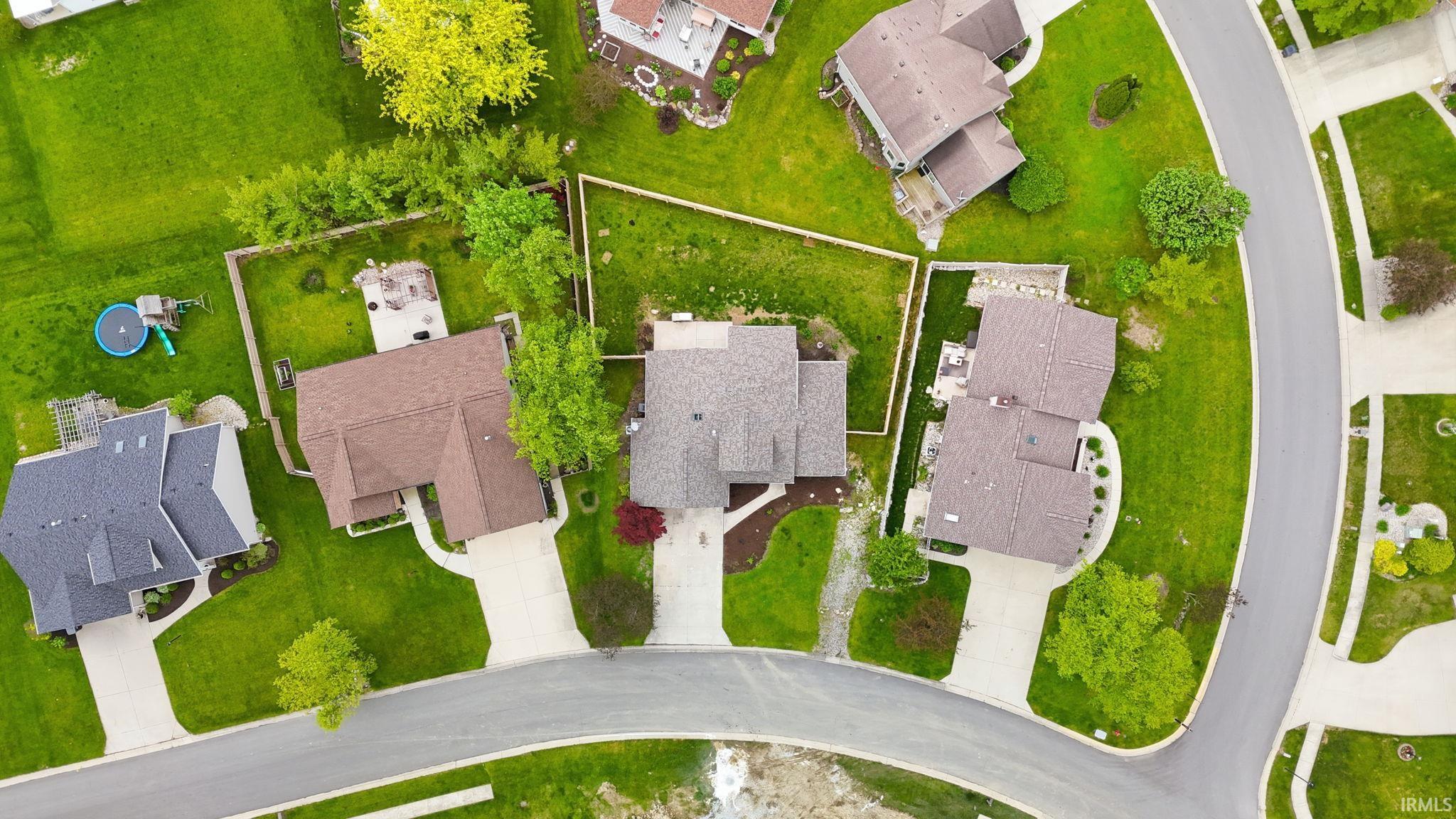 Aerial perspective showcasing a residential property with a brown shingle roof, a concrete driveway, and a verdant lawn