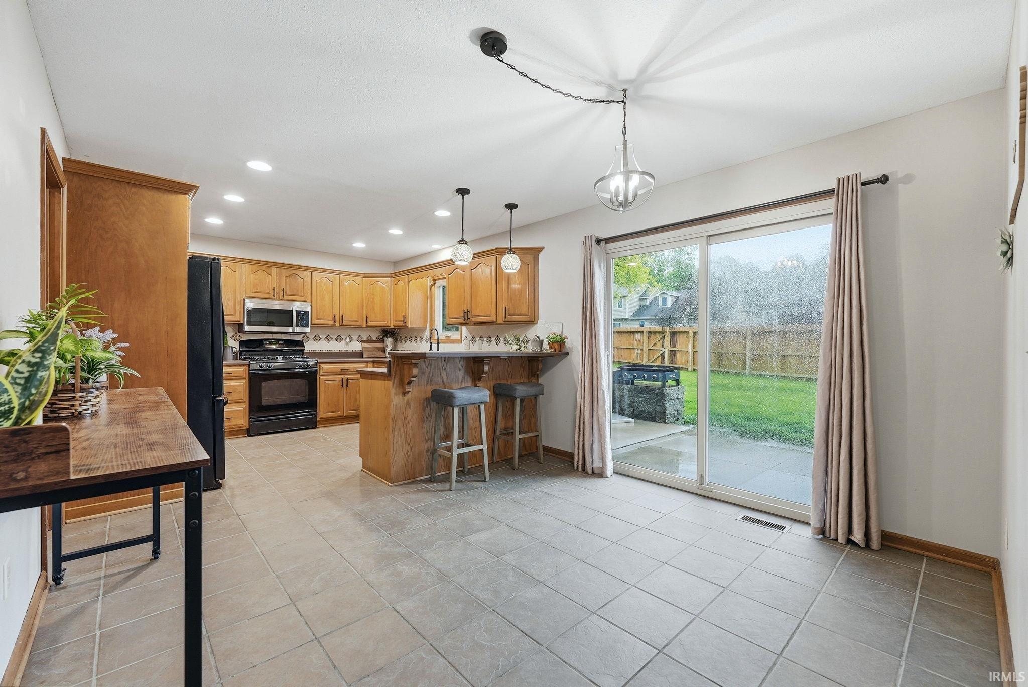 Kitchen and dining area featuring ceramic tile flooring, oak cabinetry, and black appliances