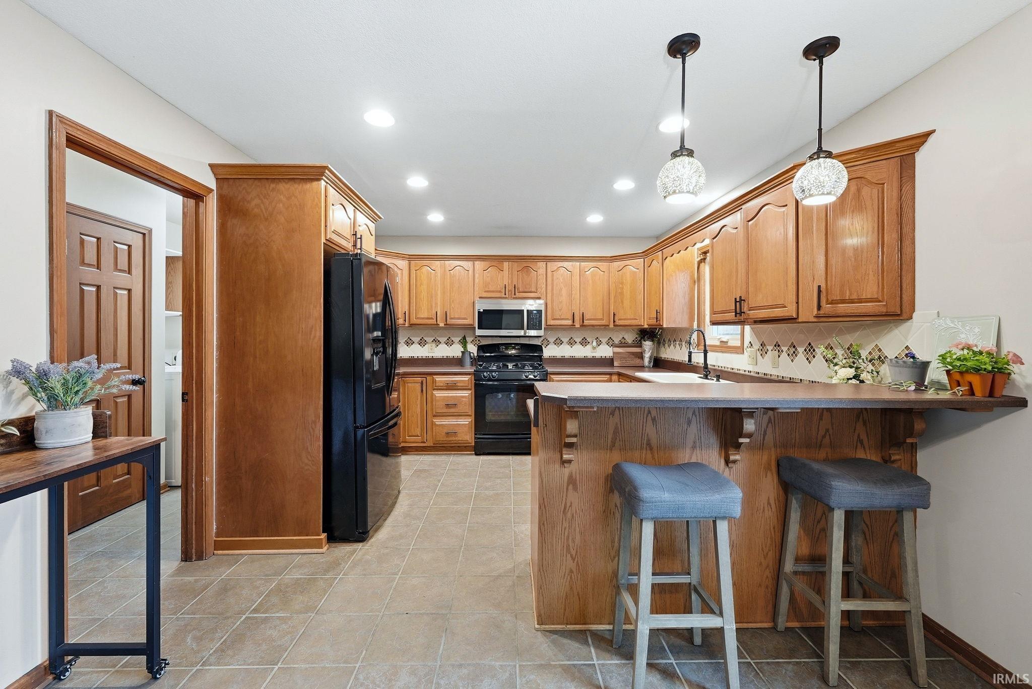 Kitchen featuring wood-finish cabinetry, black appliances, a breakfast bar with pendant lighting, recessed ceiling lights, and tile flooring