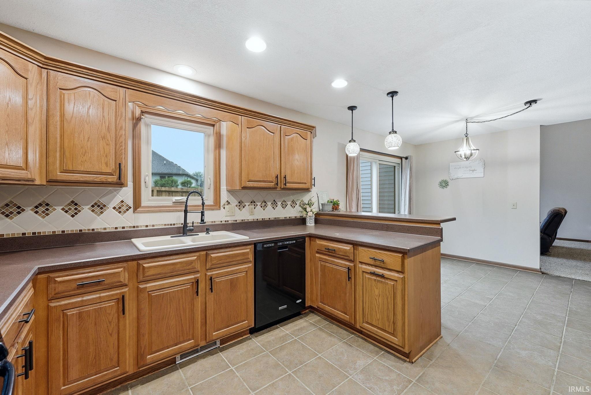 Kitchen featuring wood cabinetry, a dual-basin sink with a gooseneck faucet, black appliances, and a mosaic tile backsplash