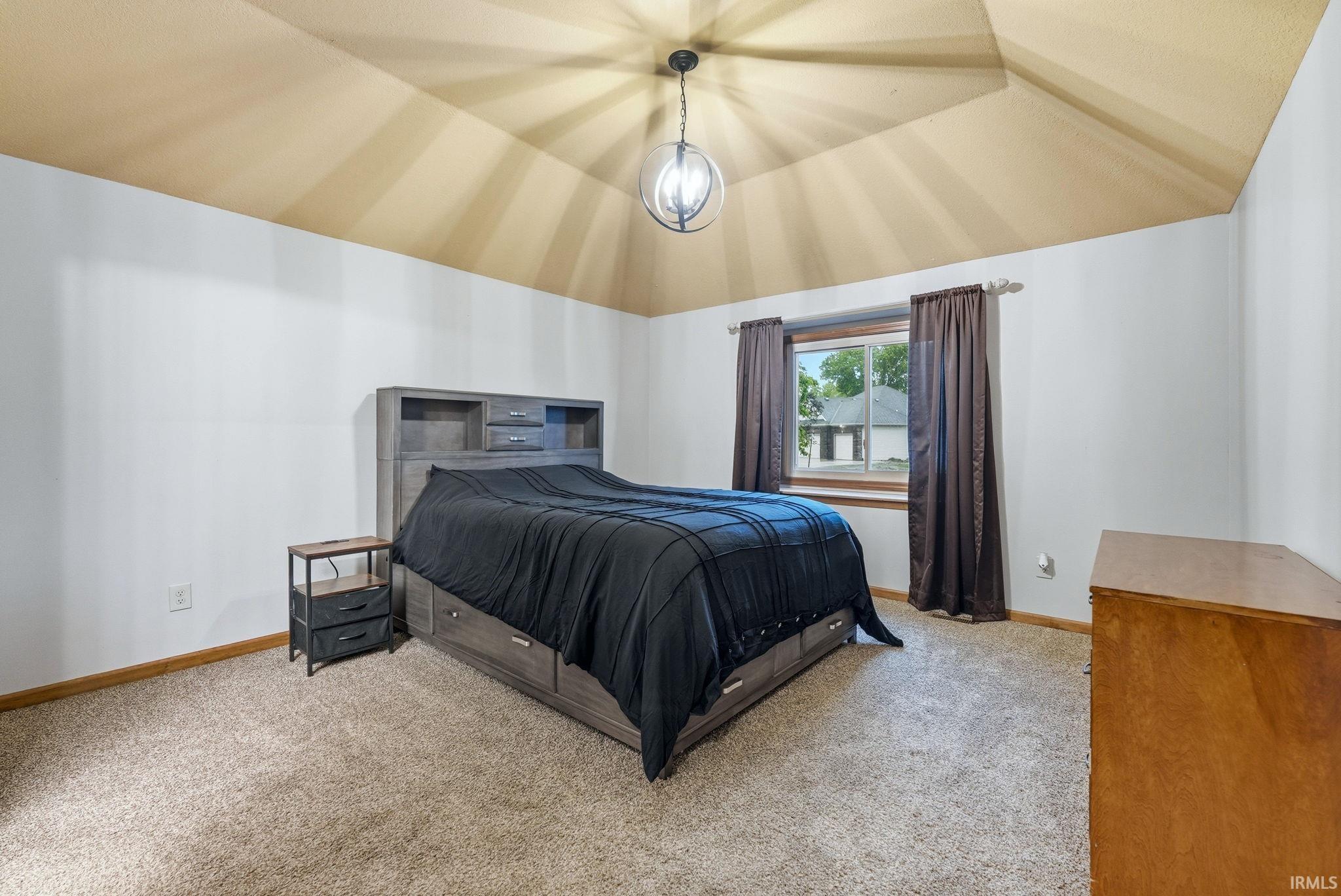 Vaulted ceiling featuring a central orb light fixture, carpet flooring, and a single window with wood trim