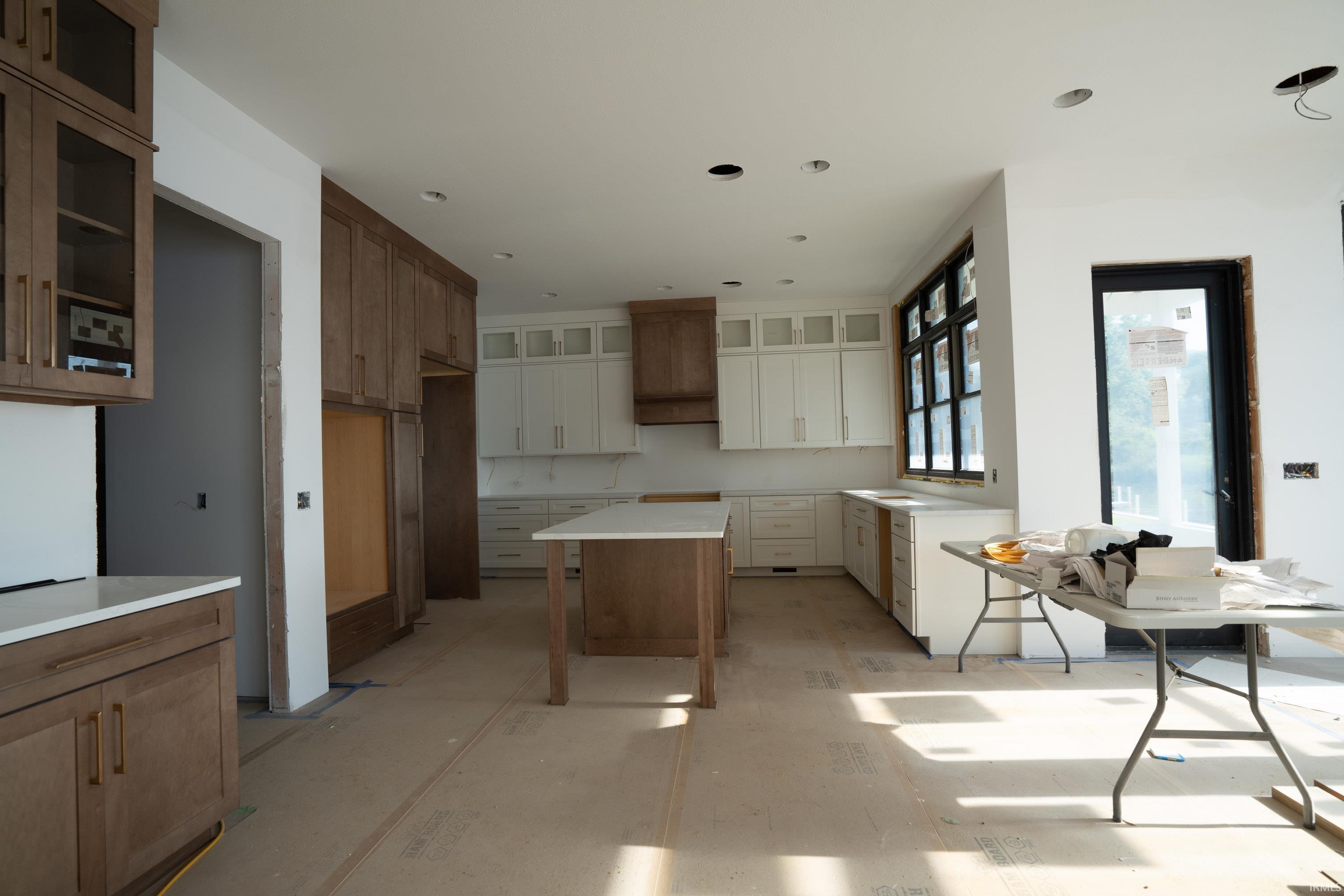 Spacious kitchen featuring two-tone cabinetry, a central island with a solid surface countertop, large black-framed windows, and recessed lighting