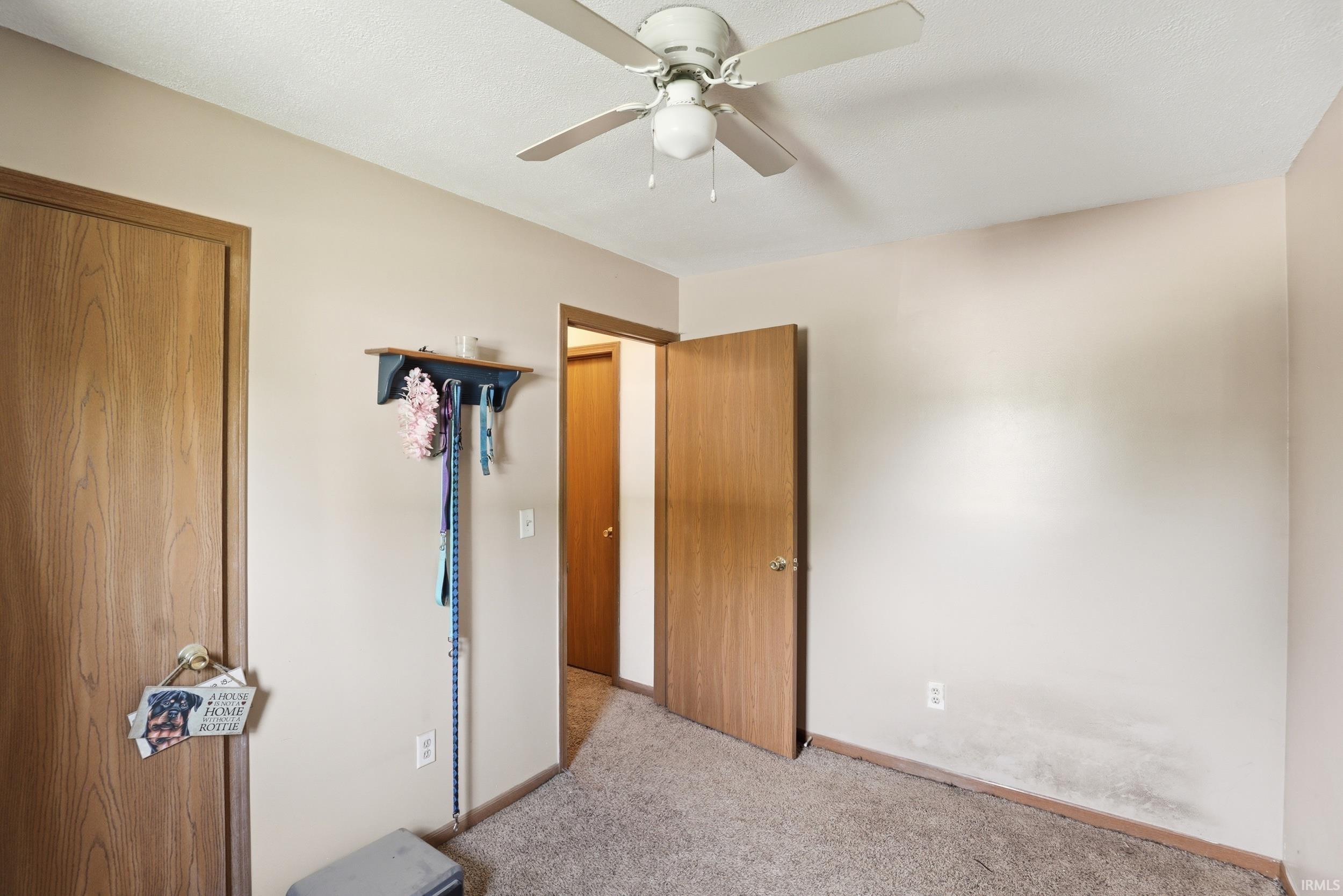 Room featuring light neutral wall paint, wood-finish doors, ceiling fan with integrated lighting, and carpet flooring