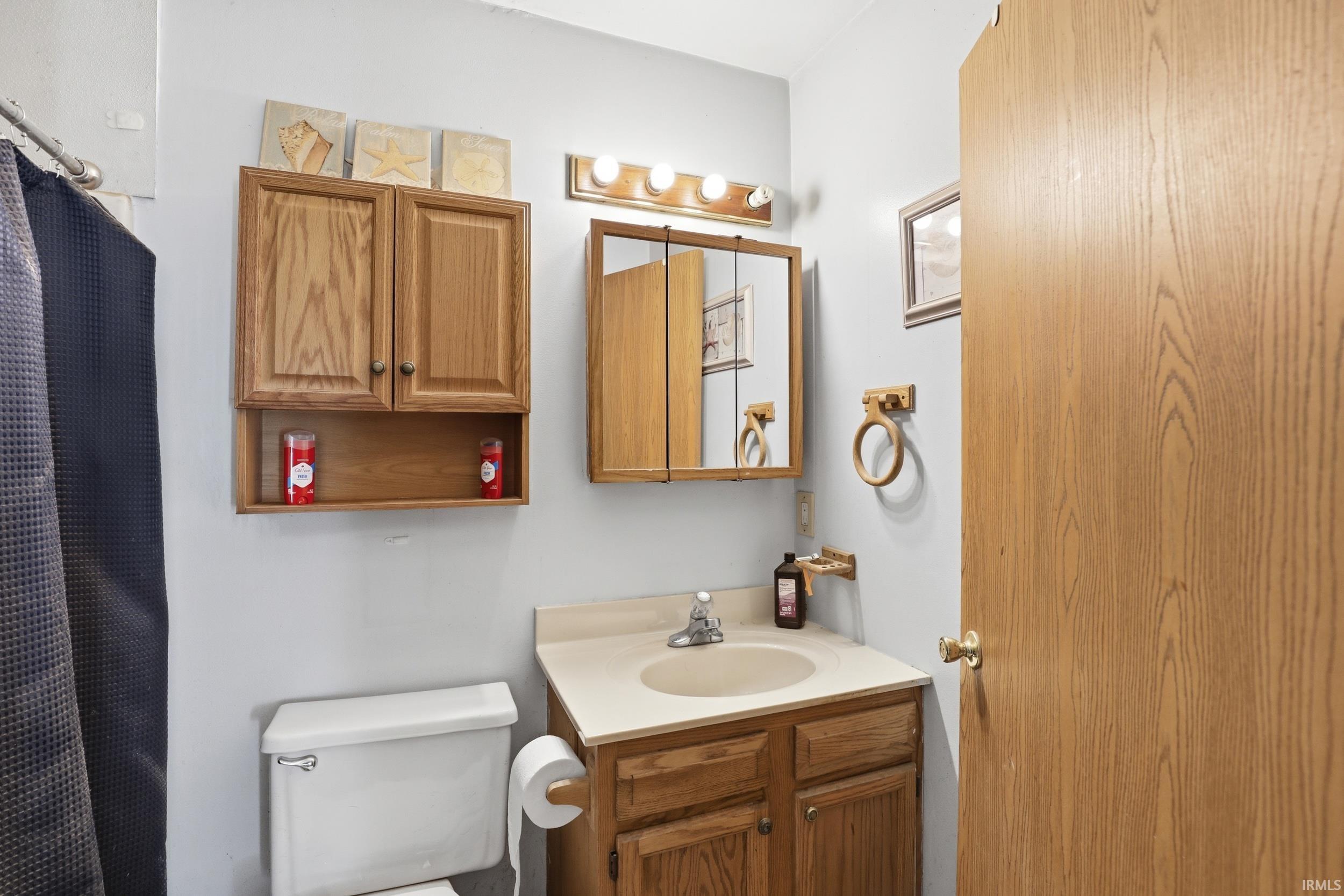 Bathroom featuring a light wood-finish vanity with an integrated sink, matching overhead cabinet with open shelving, and medicine cabinet