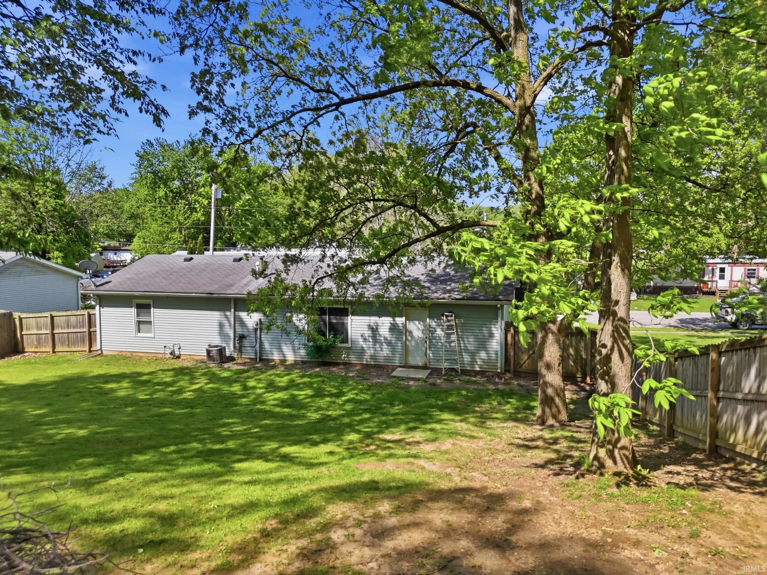 Expansive backyard featuring a manicured lawn, established trees, and a full privacy fence