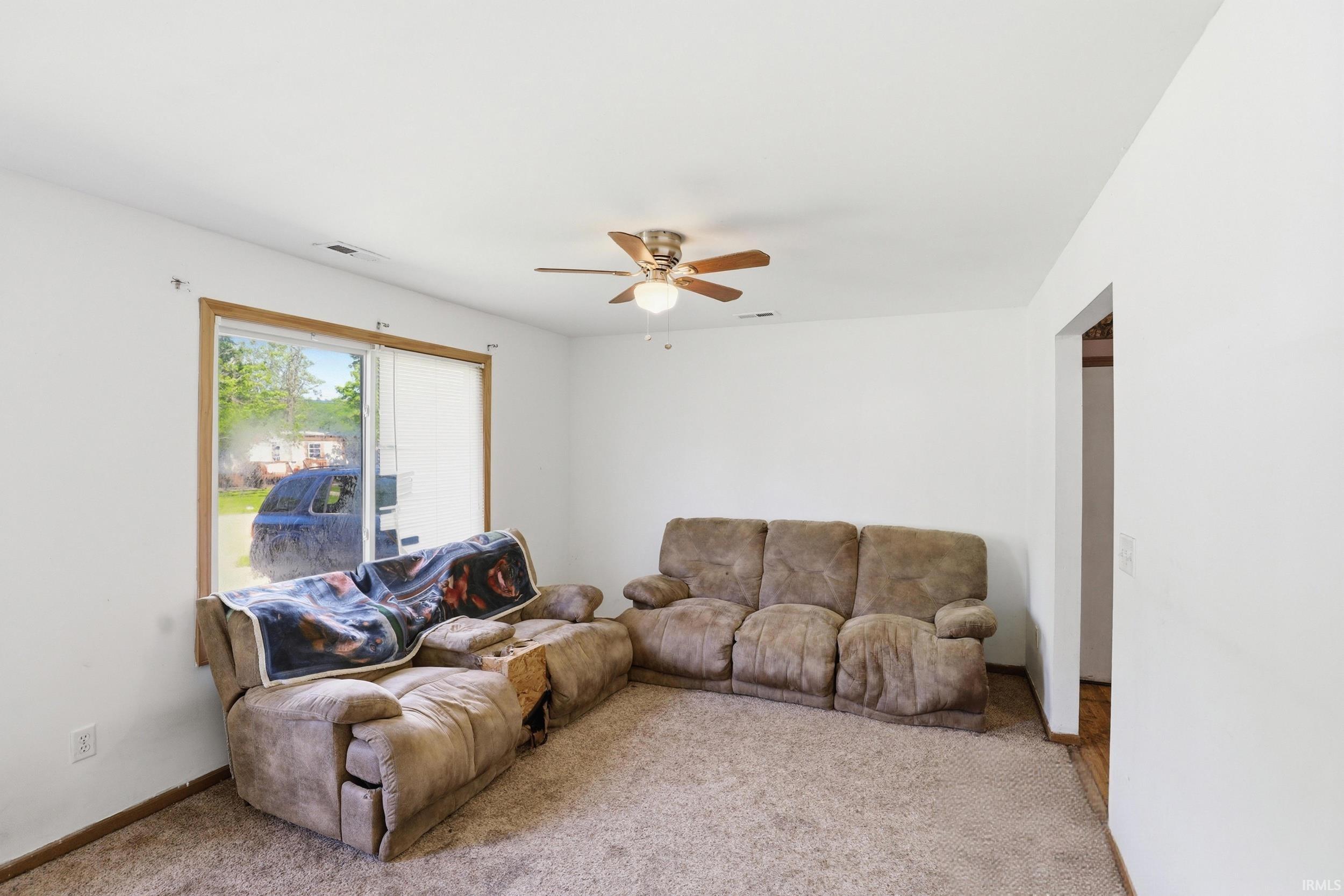 Carpeted living space featuring a ceiling fan, white walls, and wood-finish baseboards