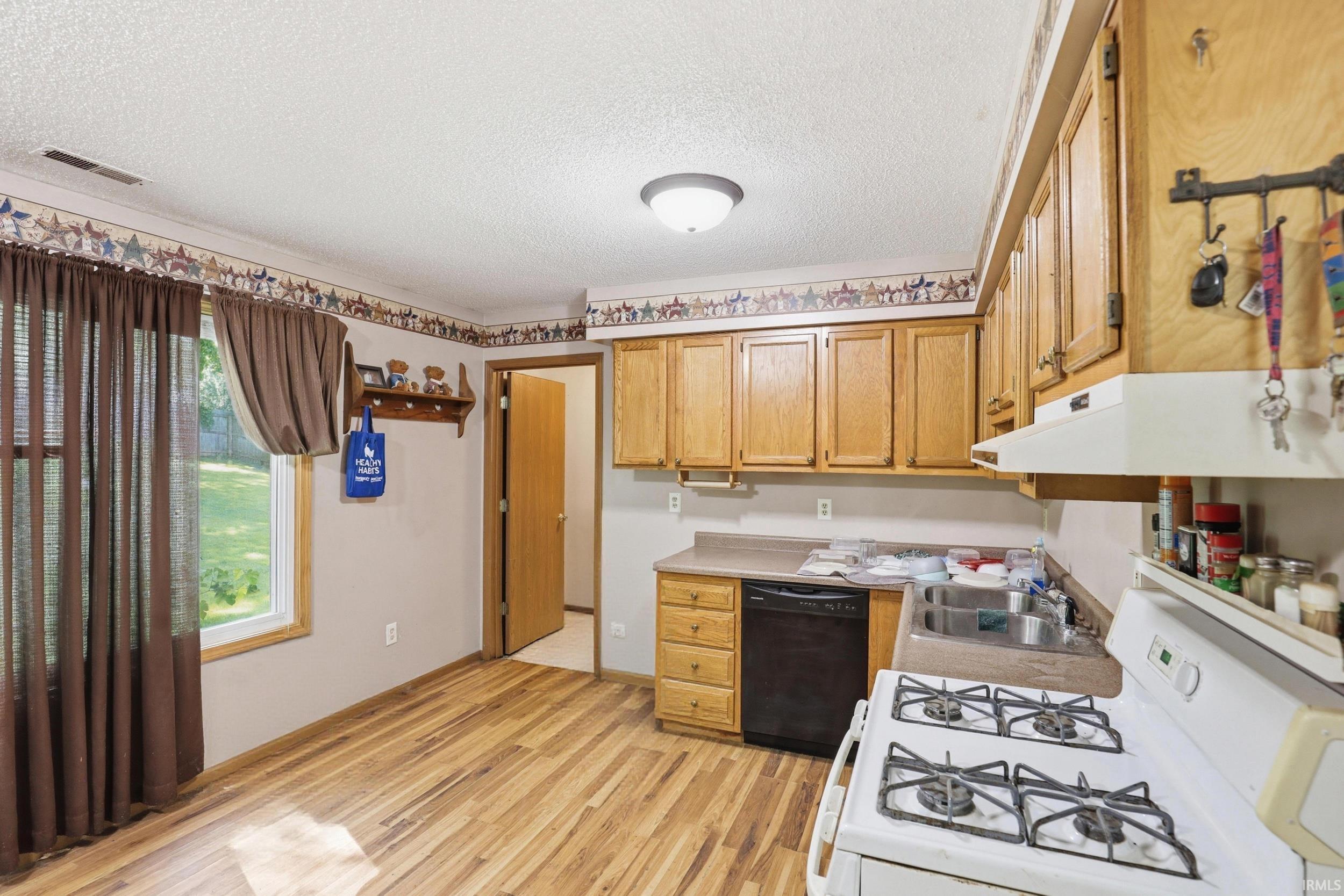 Kitchen featuring light wood-finish cabinetry, a white gas range with a range hood, and a black dishwasher
