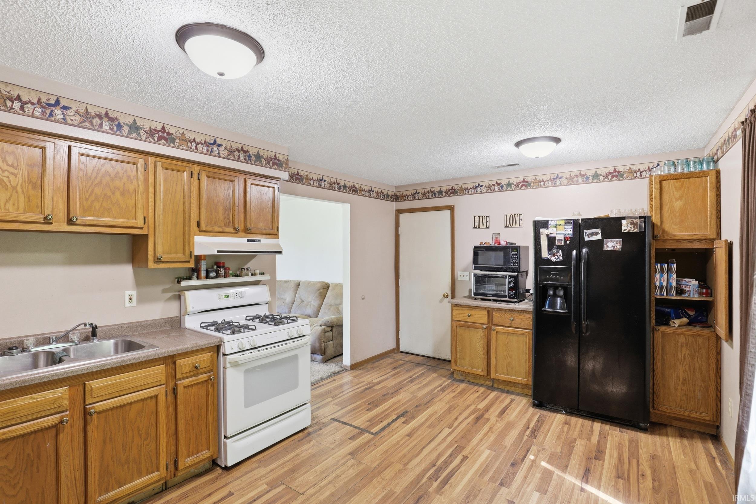Kitchen featuring wood-finish flooring, natural wood cabinetry, and a white gas range with overhead vent