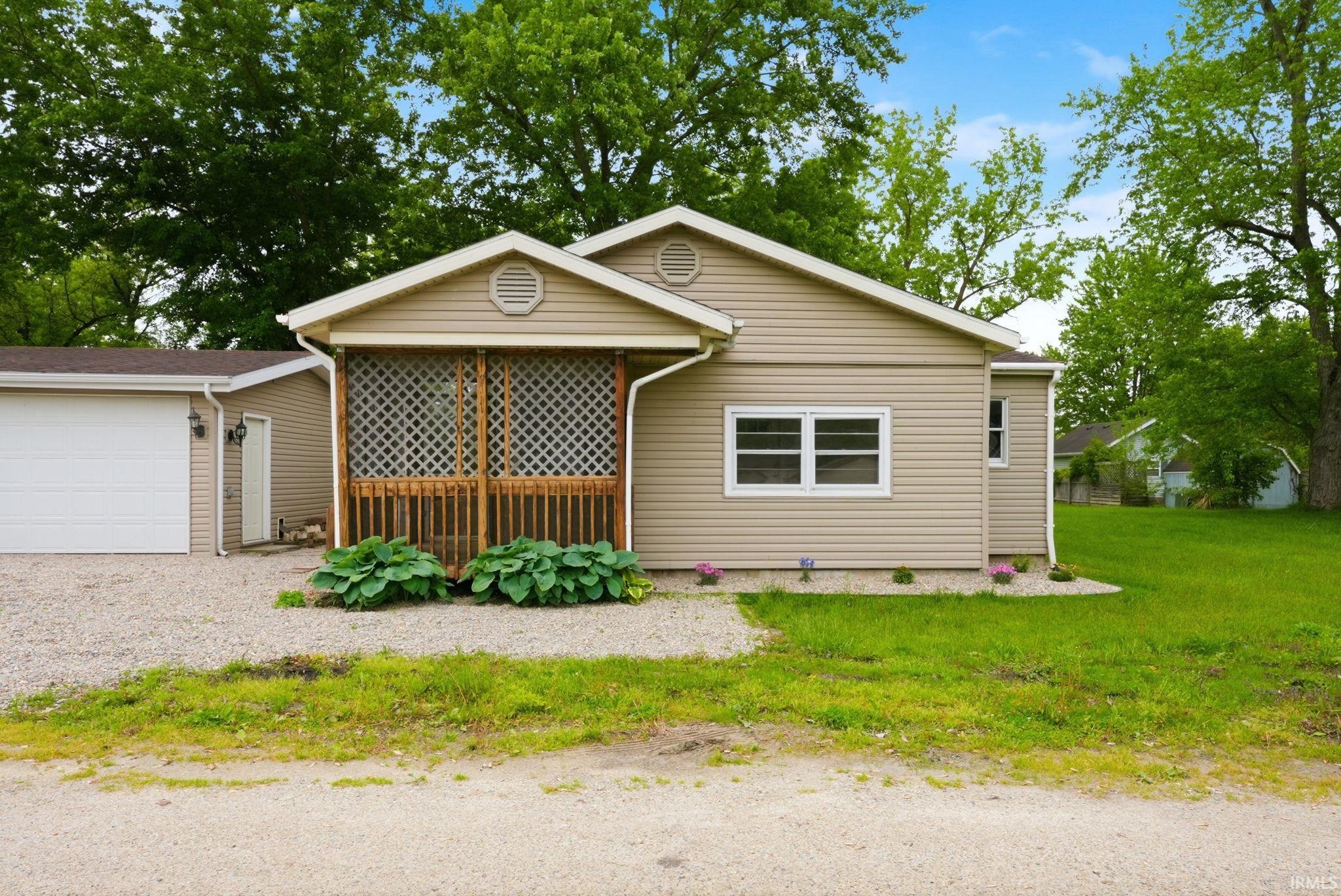 Single-story residence featuring tan horizontal siding, a screened porch with wood-finish railing and lattice, a white garage door, and white frame windows