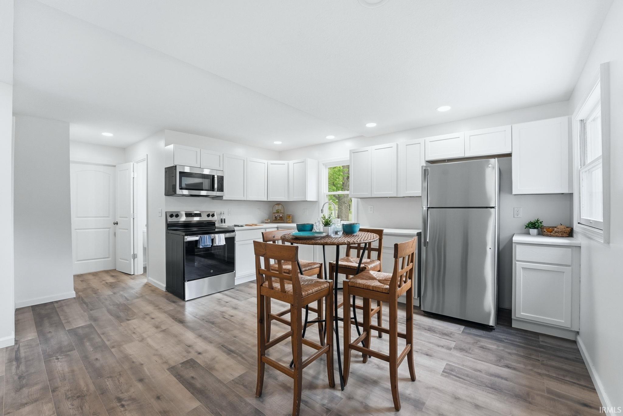 Kitchen featuring white shaker-style cabinetry, stainless steel appliances, wood-finish flooring, recessed lighting, and a window