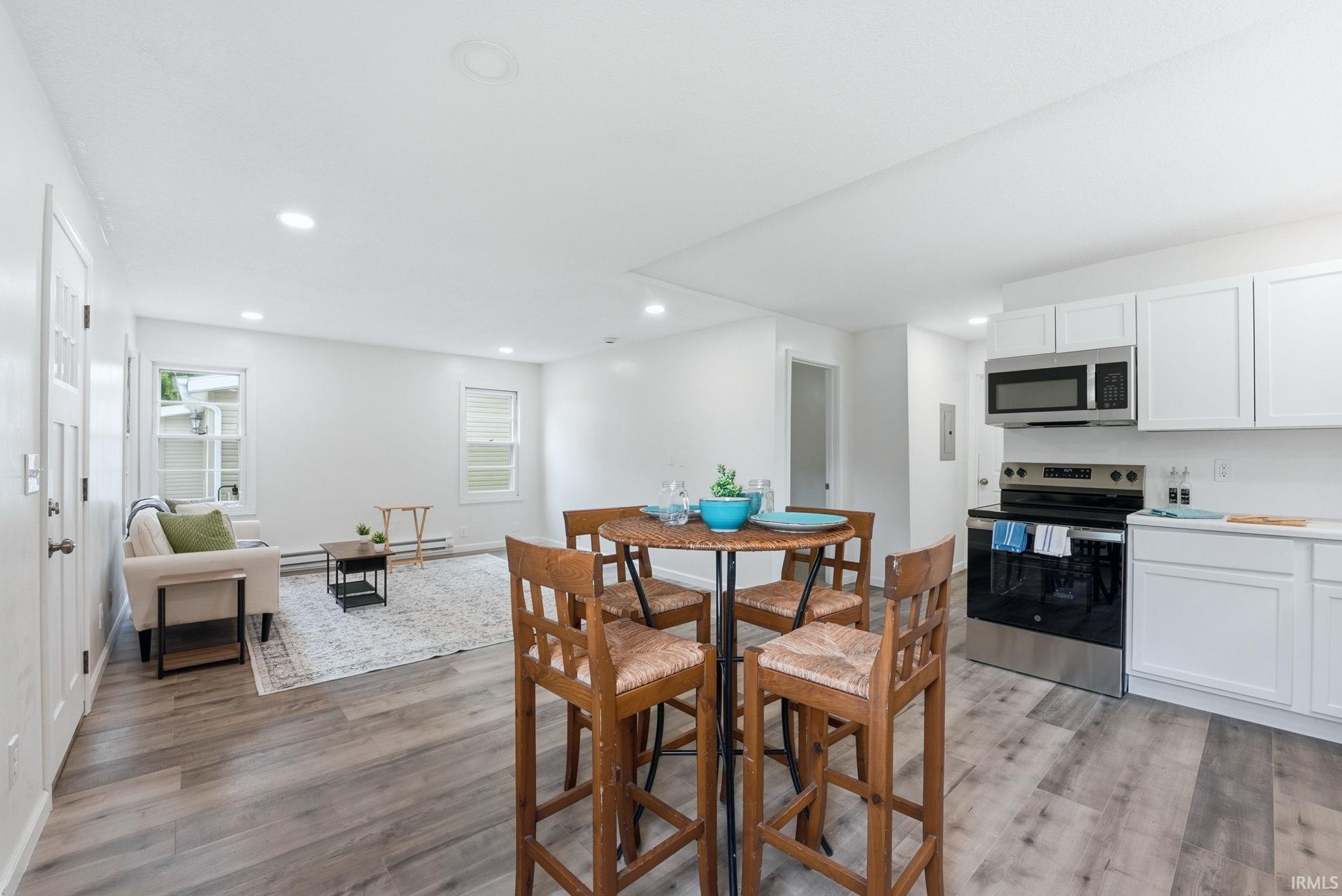 Open-concept living space featuring wood-finish flooring, recessed lighting, white walls, white shaker-style kitchen cabinetry, and stainless steel kitchen appliances