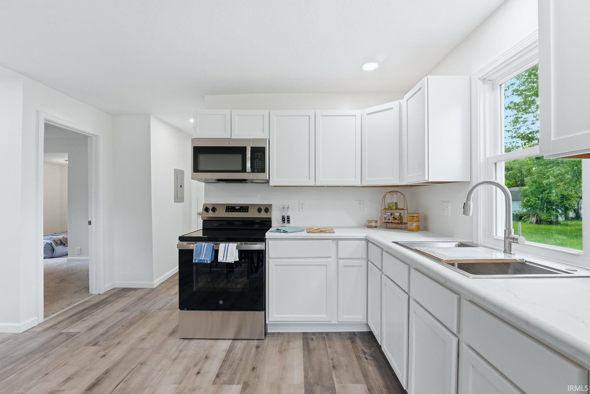 Modern kitchen featuring wood-finish flooring, white cabinetry, a stainless steel range with overhead microwave, a deep single-basin sink, and white countertops