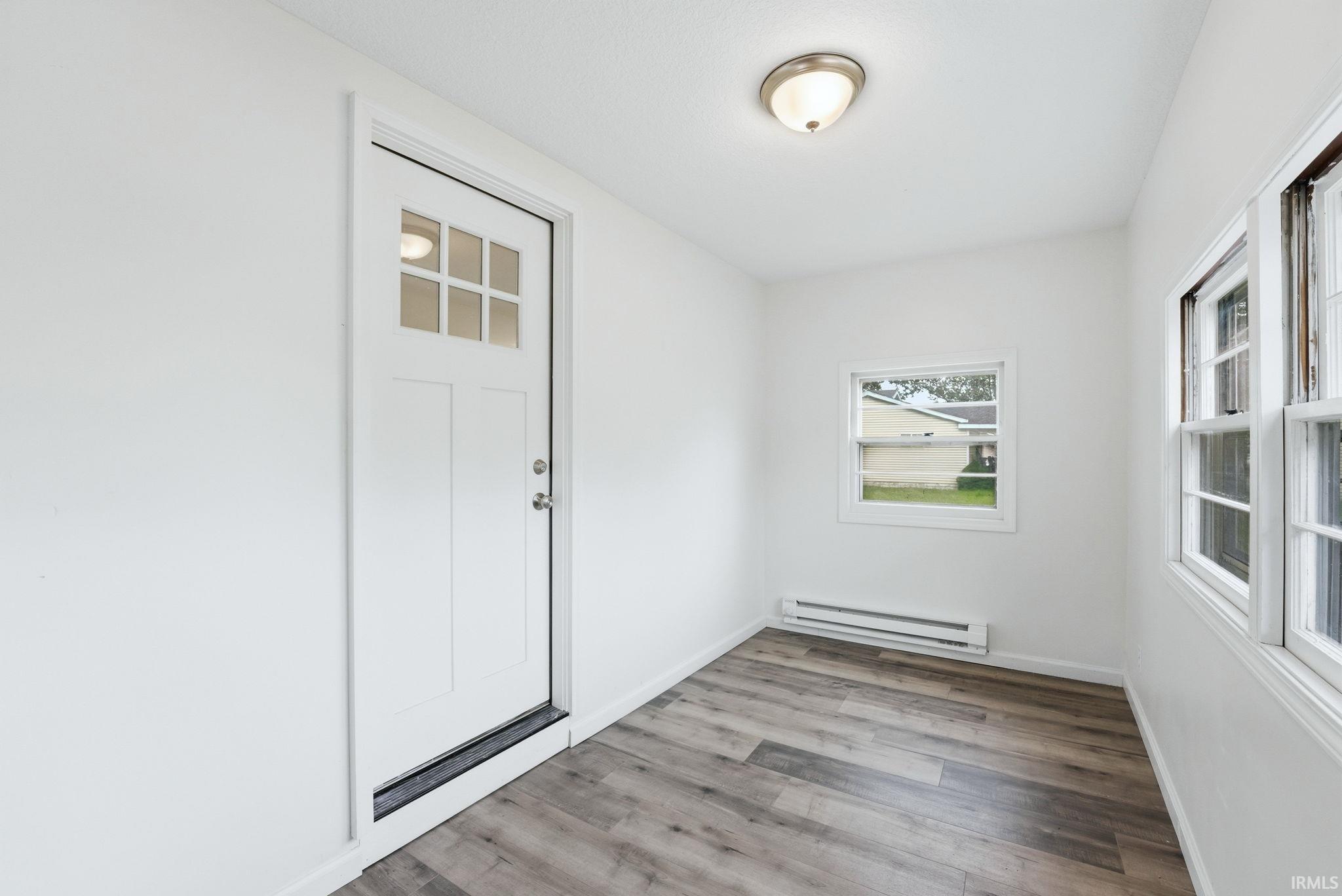 Entryway featuring a paneled door with divided lites, wood-finish flooring, multiple windows, a baseboard heater, and a flush-mount ceiling light fixture