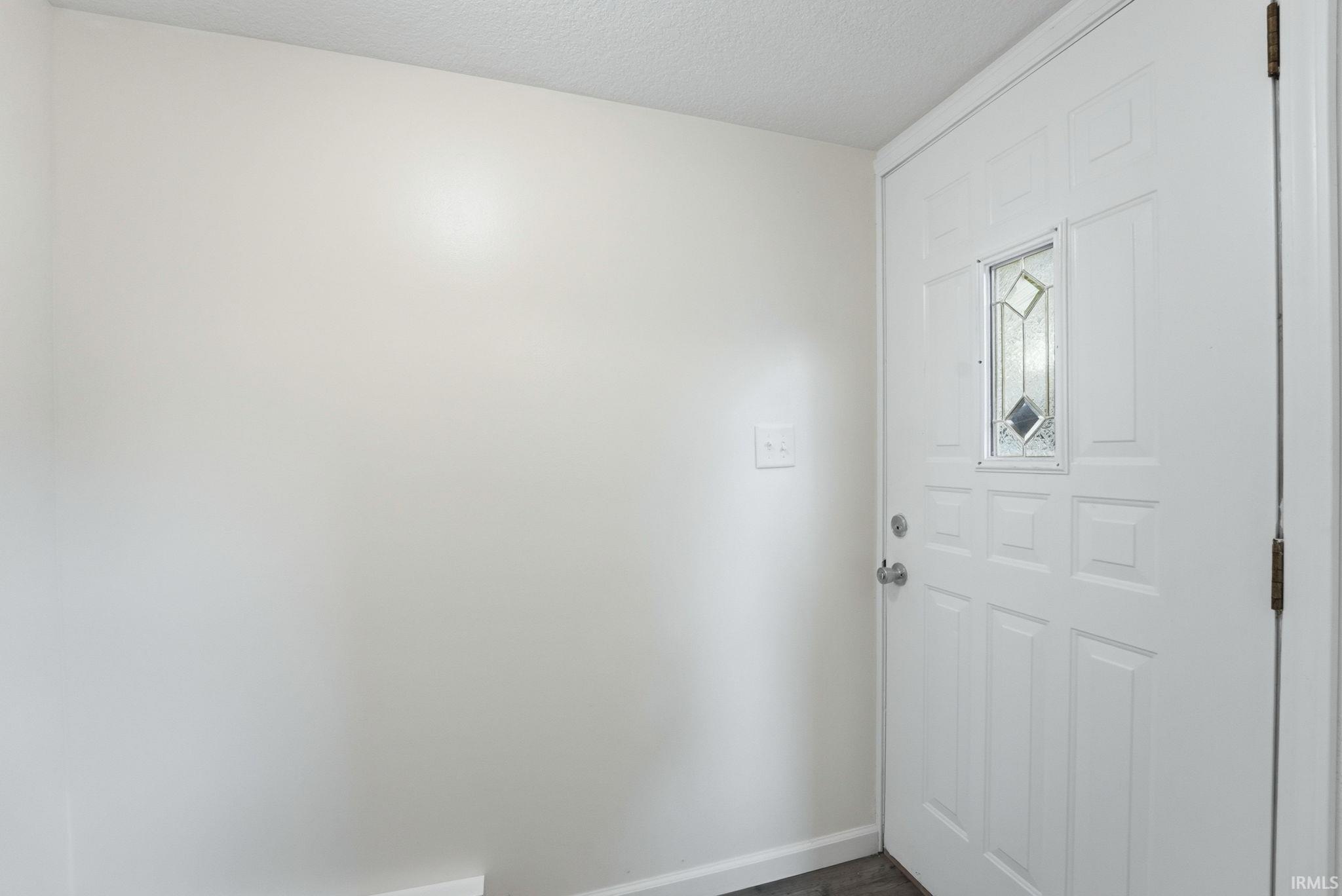 White paneled entry door with decorative glass insert, chrome hardware, and dark wood-finish flooring