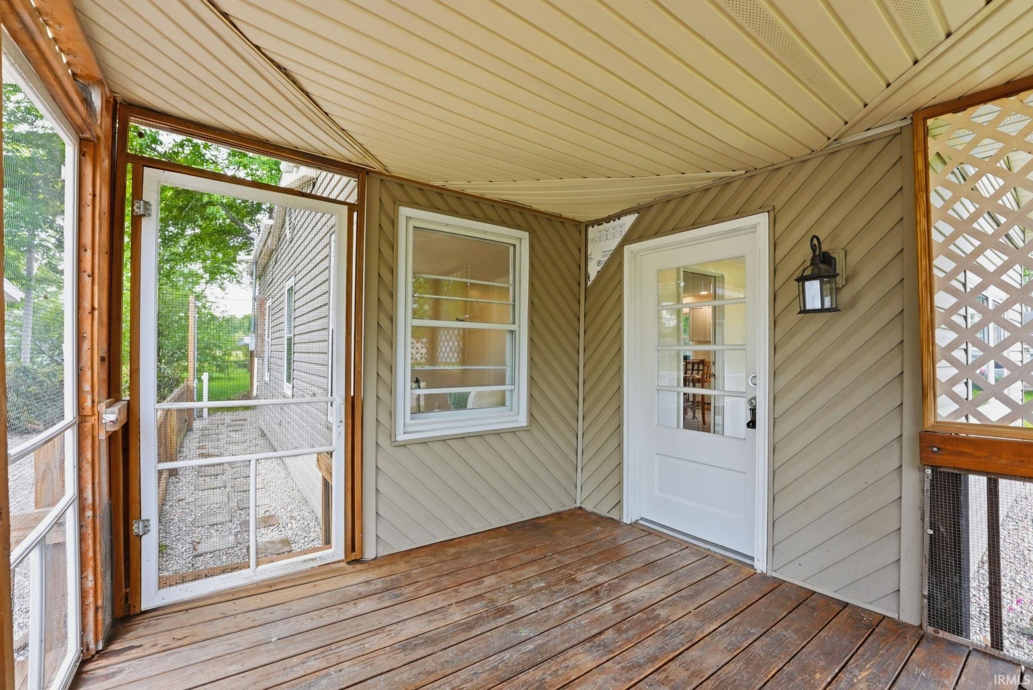 Screened porch with wood-finish flooring, diagonal siding, and a white paneled door with glass inserts