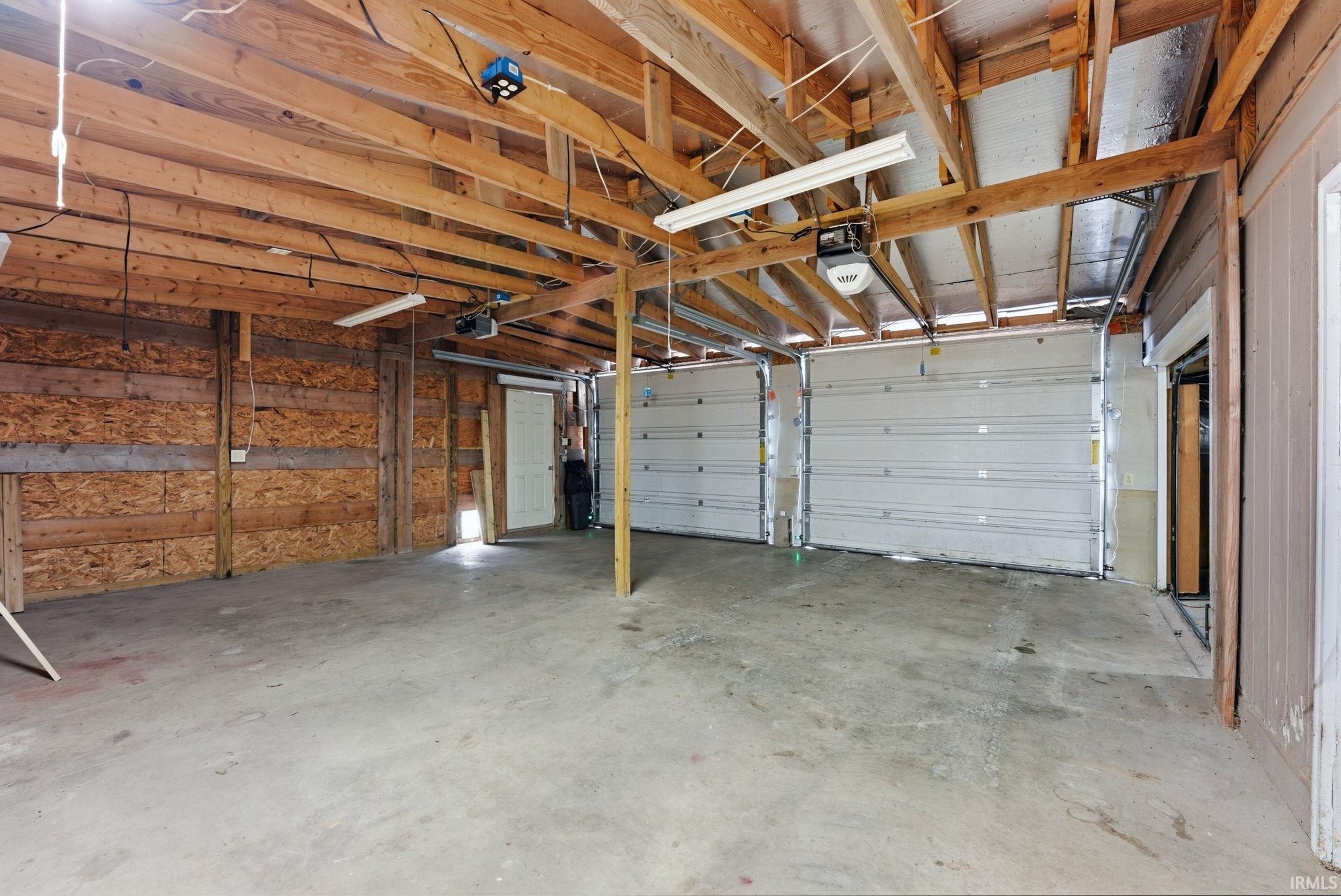 Spacious garage featuring two overhead doors, exposed wood framing, concrete flooring, and fluorescent lighting fixtures