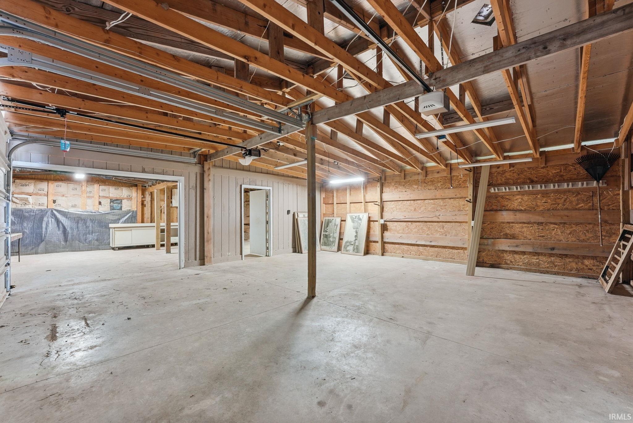 Spacious garage area featuring an exposed beam ceiling, concrete flooring, and a roll-up garage door mechanism