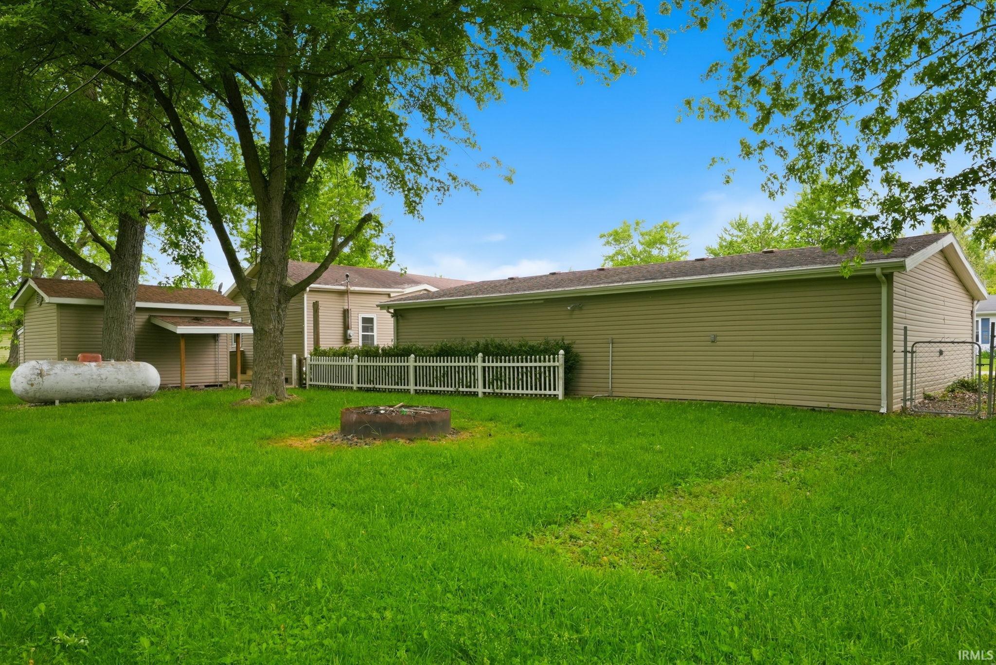 Expansive green lawn with mature trees, a detached garage with vinyl siding, and a white picket fence