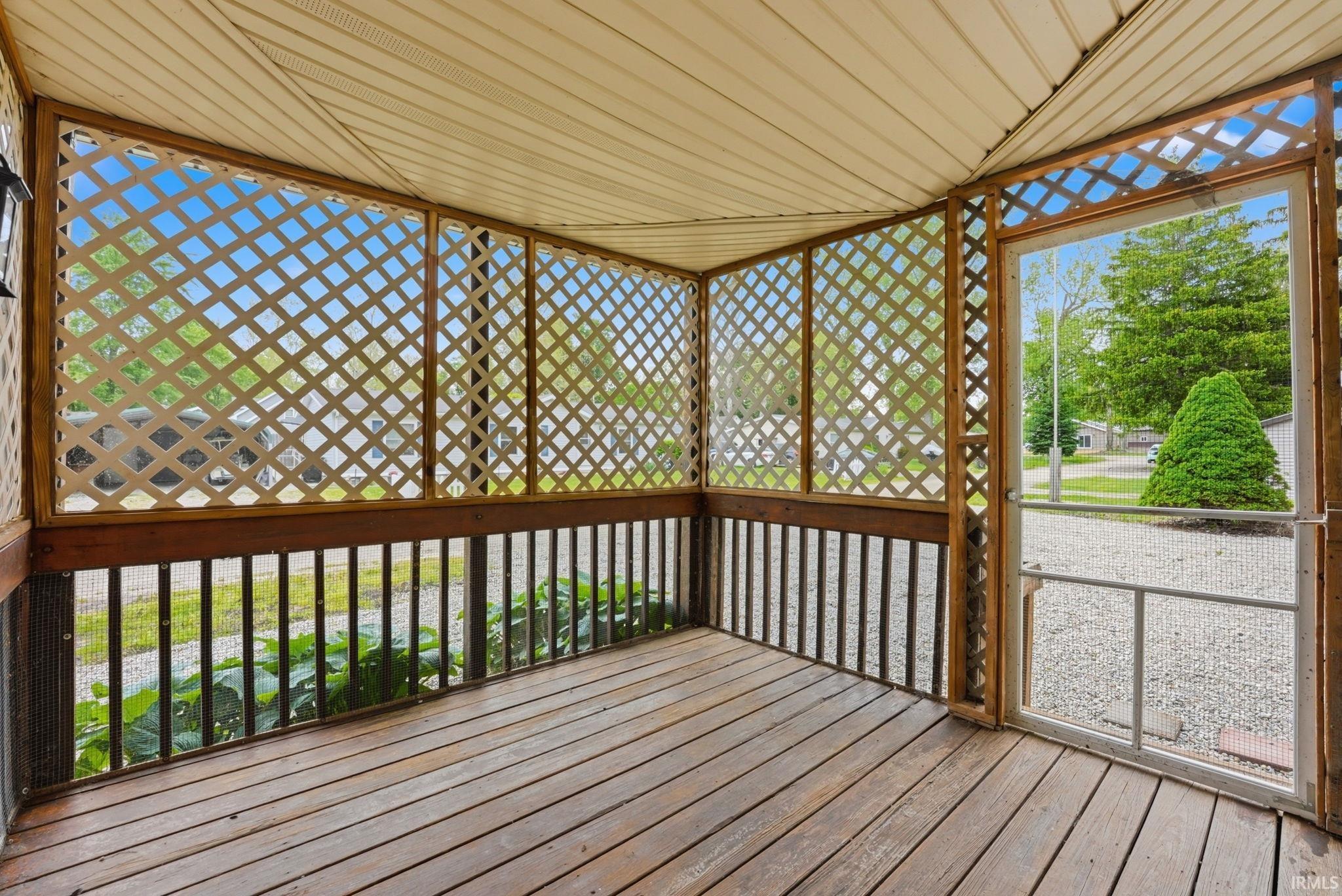 Enclosed porch featuring wood-finish flooring, white lattice panels, and a screen door
