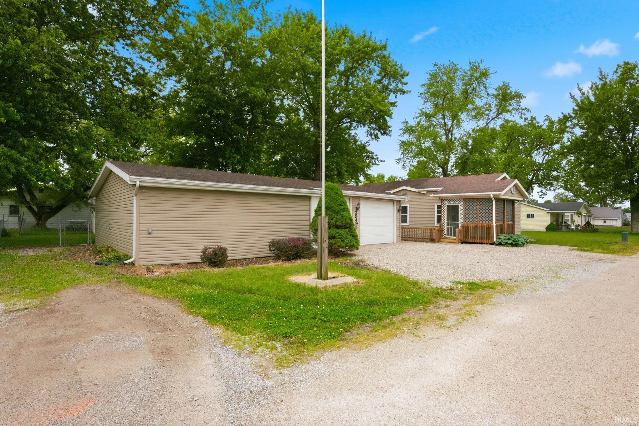 Property exterior featuring a gravel driveway, detached garage with siding, and mature trees