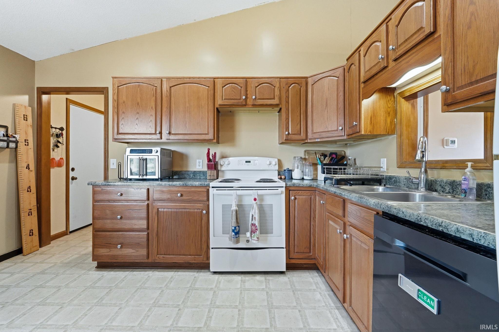 Kitchen featuring wood cabinetry, laminate countertops, a double basin stainless steel sink, and a white electric range