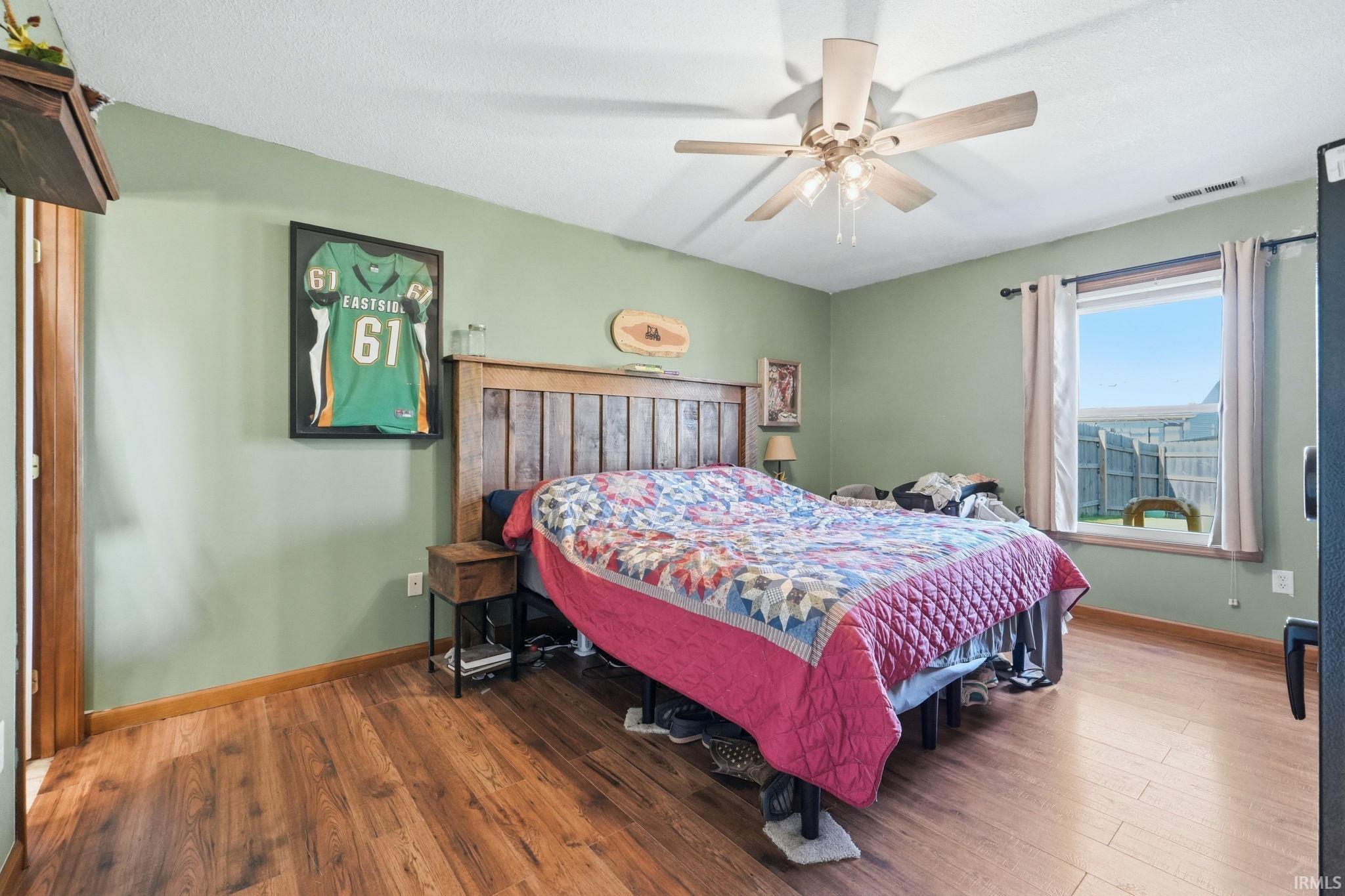 Bedroom featuring wood-finish flooring, a ceiling fan, and a window with white trim