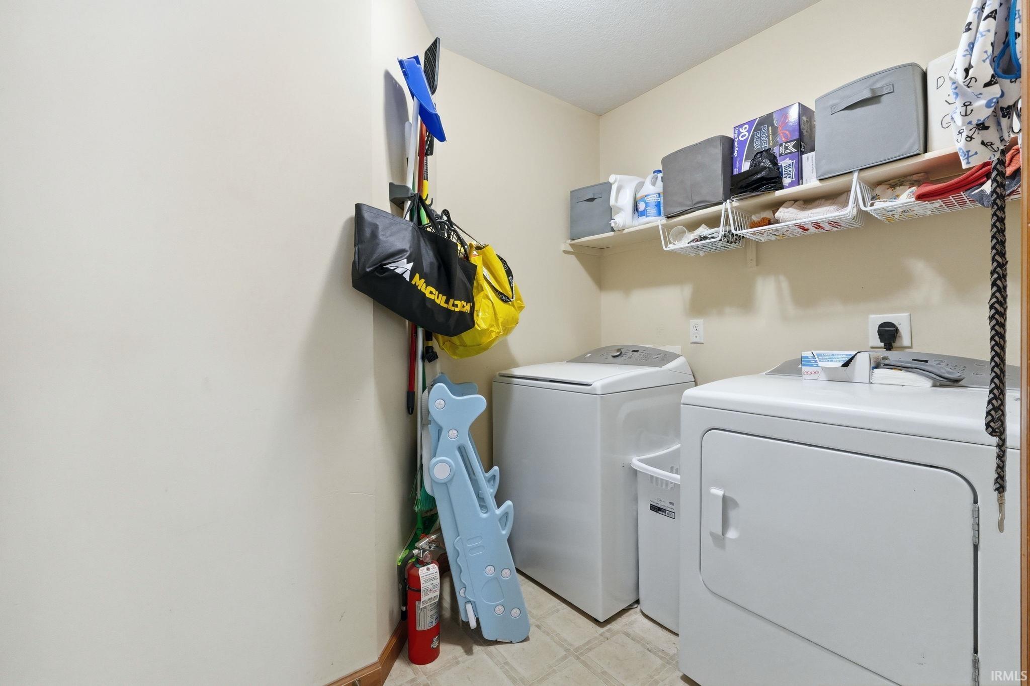 Dedicated laundry area featuring a washer and dryer, neutral wall paint, and overhead shelving for organization