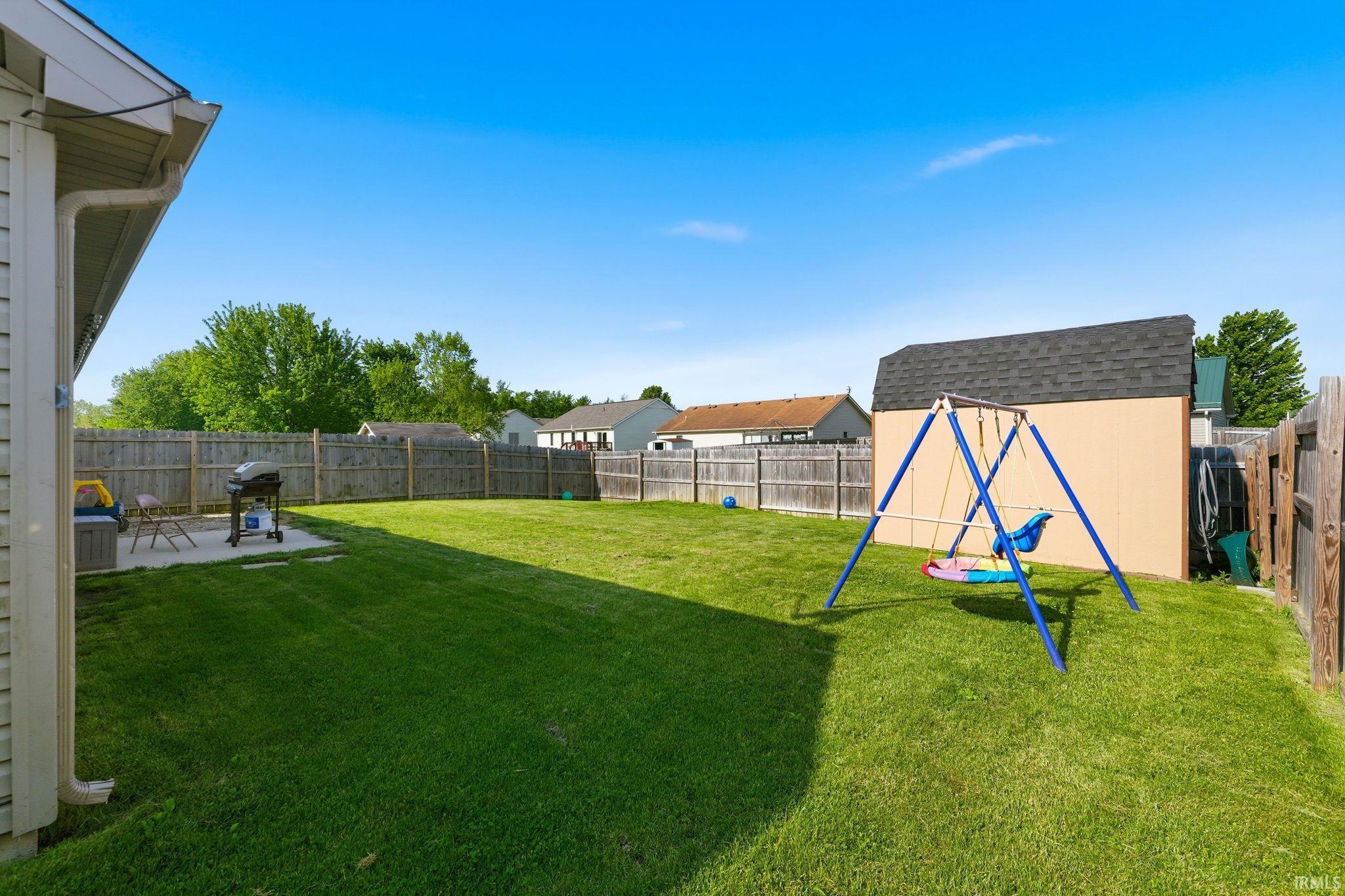 Expansive fenced backyard featuring a large green lawn, concrete patio, and a storage shed with a shingled roof