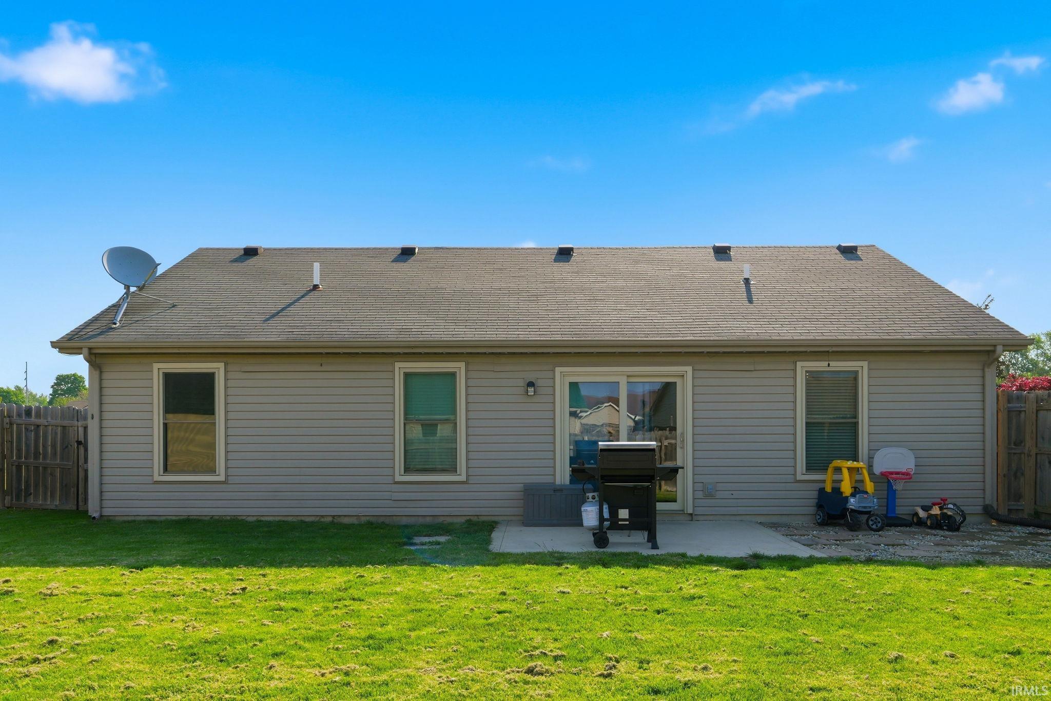 Expansive green lawn with a gray siding exterior featuring a patio, sliding glass door, and a shingled roof