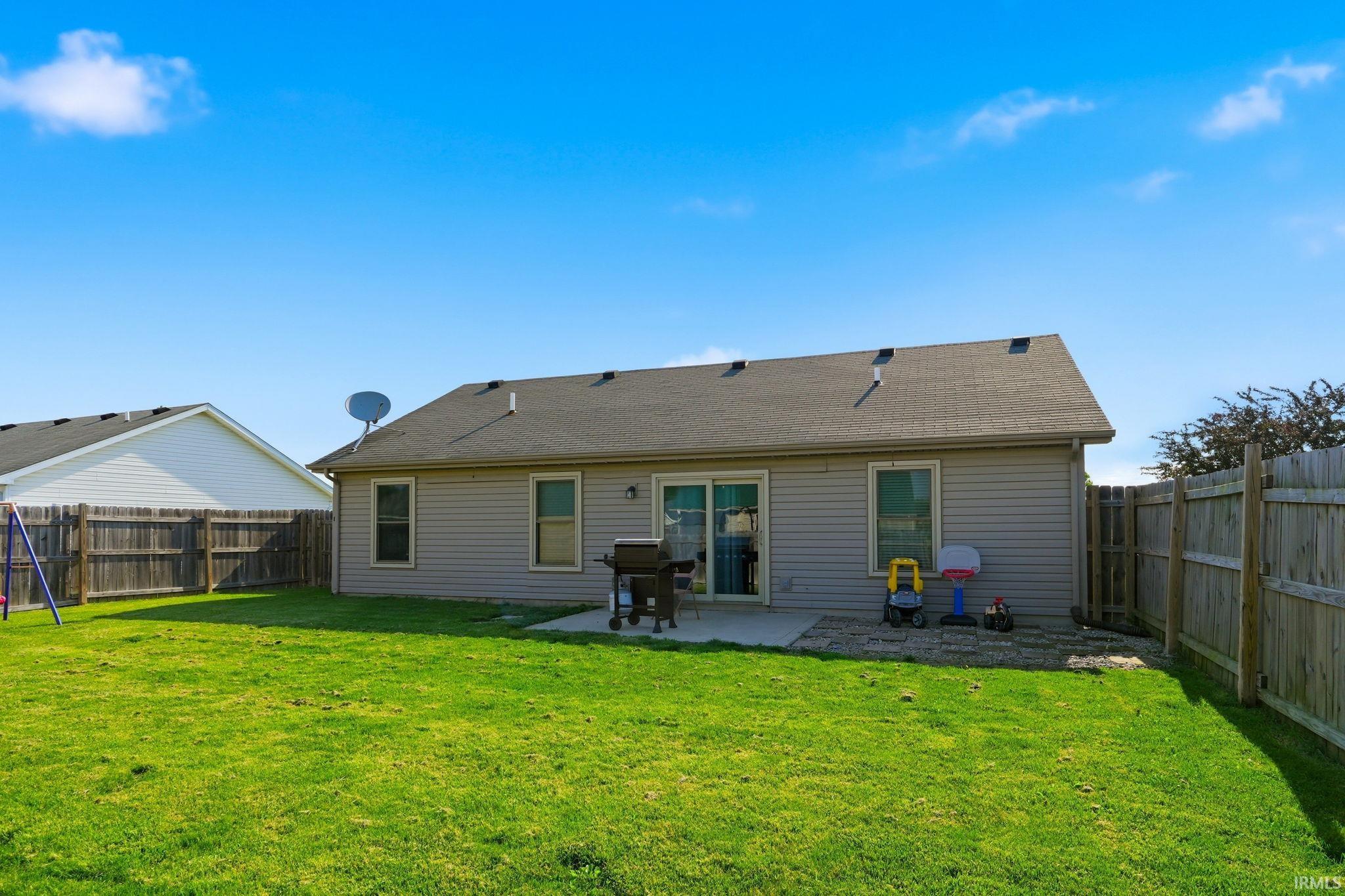 Spacious backyard featuring a manicured lawn, full privacy fencing, and a concrete patio