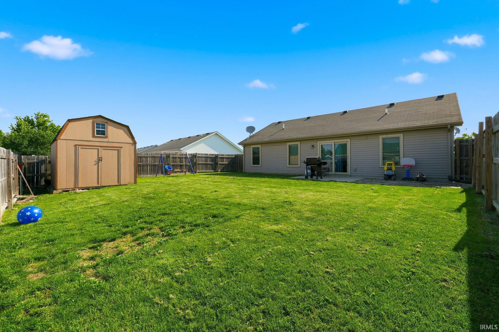 Expansive backyard featuring a privacy fence, storage shed with double doors, and a patio area