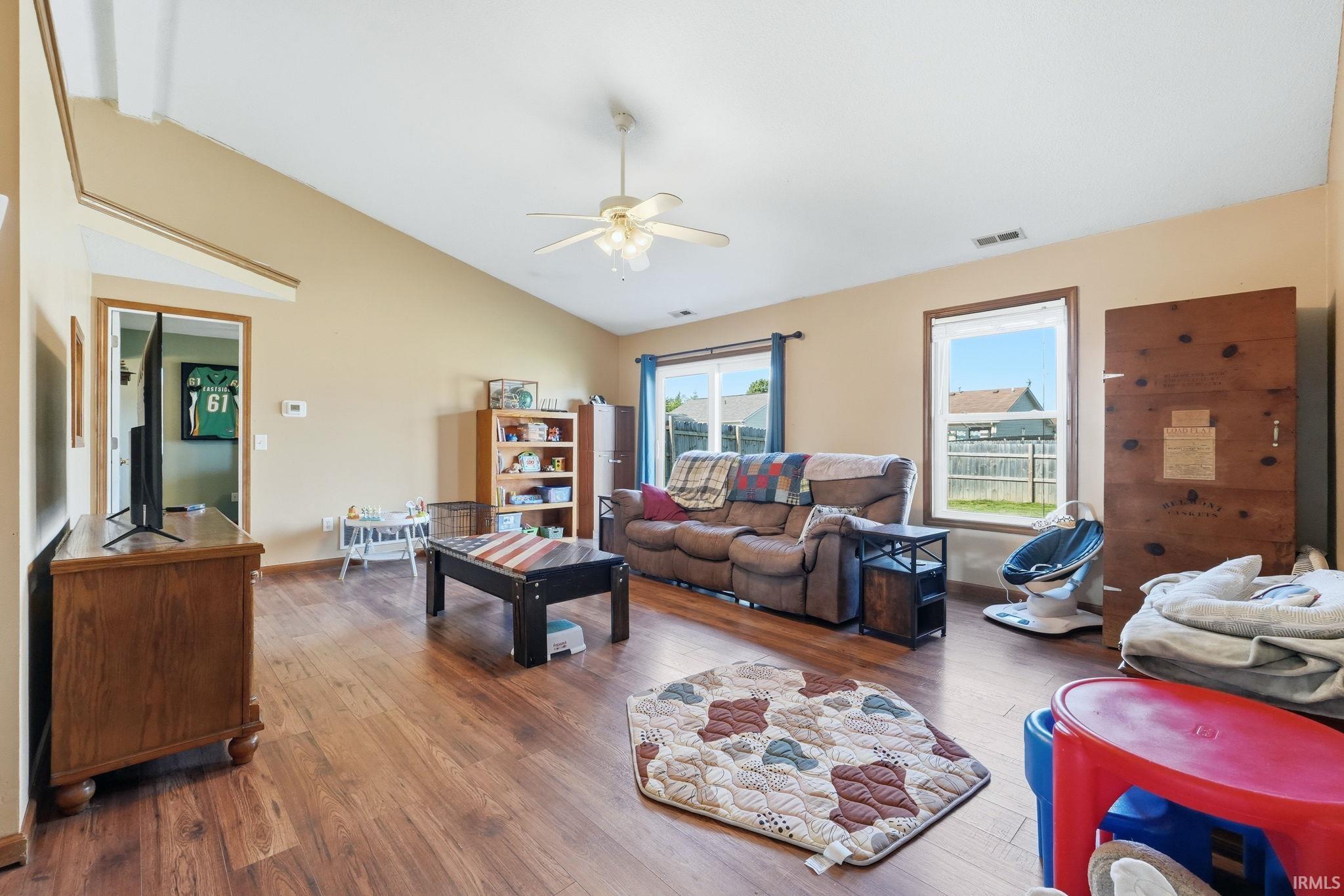 Spacious living area featuring vaulted ceilings, wood-finish flooring, and ample natural light from multiple windows