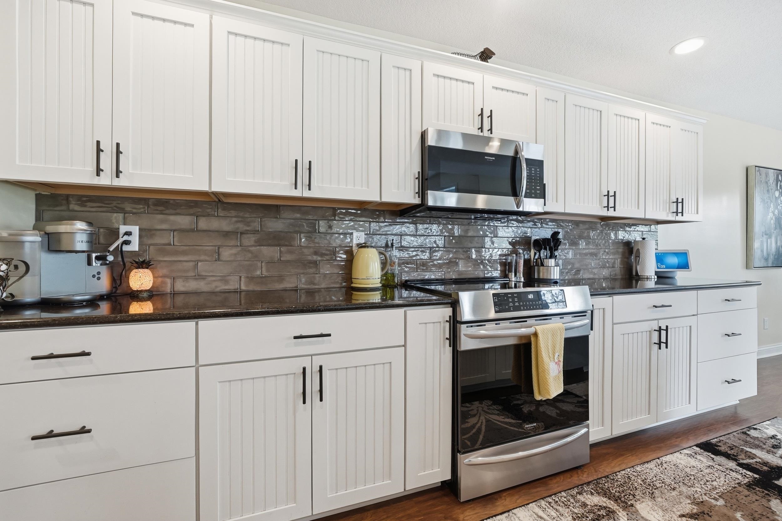 Modern kitchen featuring white shaker and beadboard cabinetry, dark countertops, a dark subway tile backsplash, and stainless steel appliances