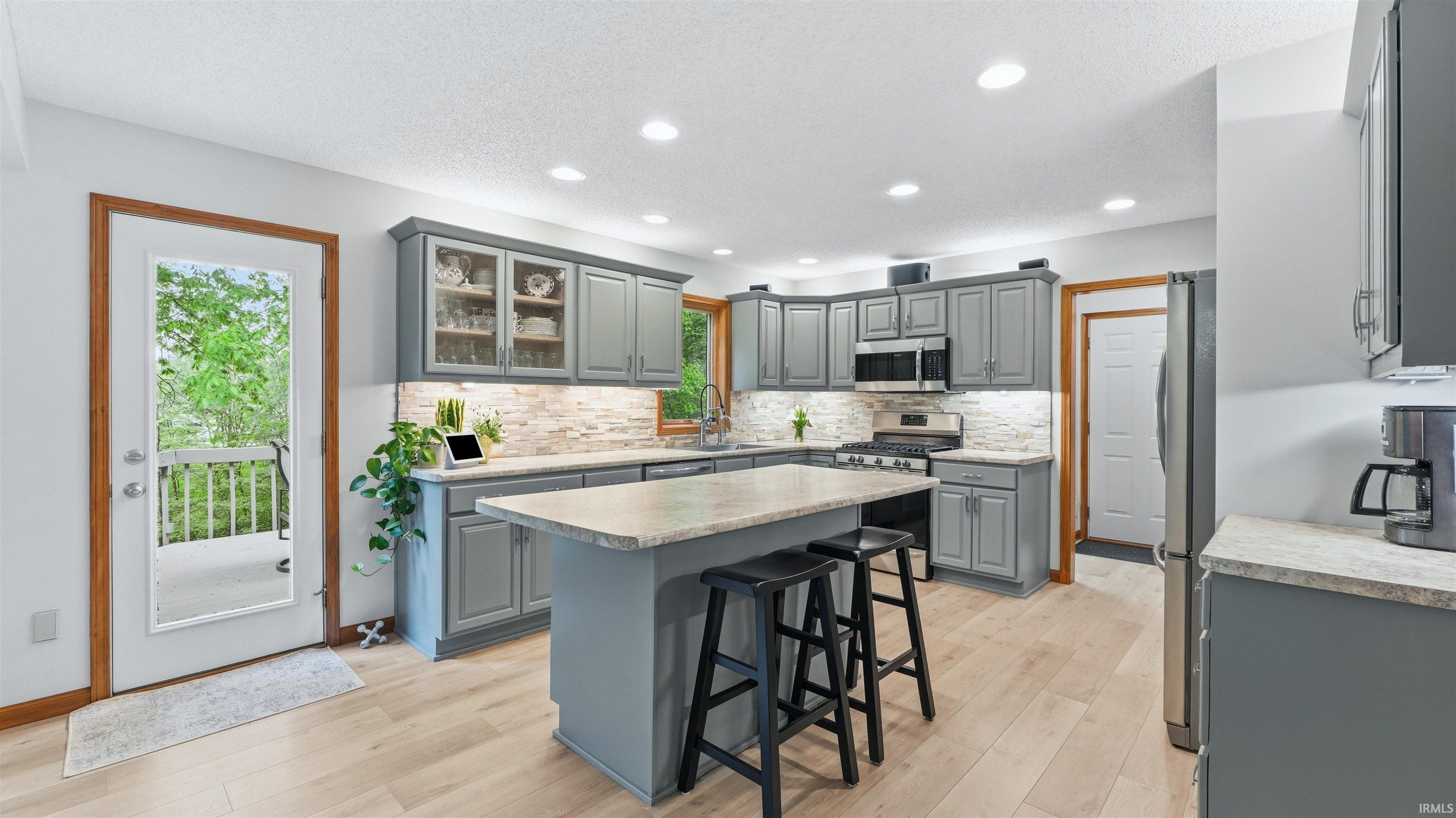 Spacious kitchen featuring light wood-finish flooring, recessed lighting, and grey cabinetry with stainless steel hardware