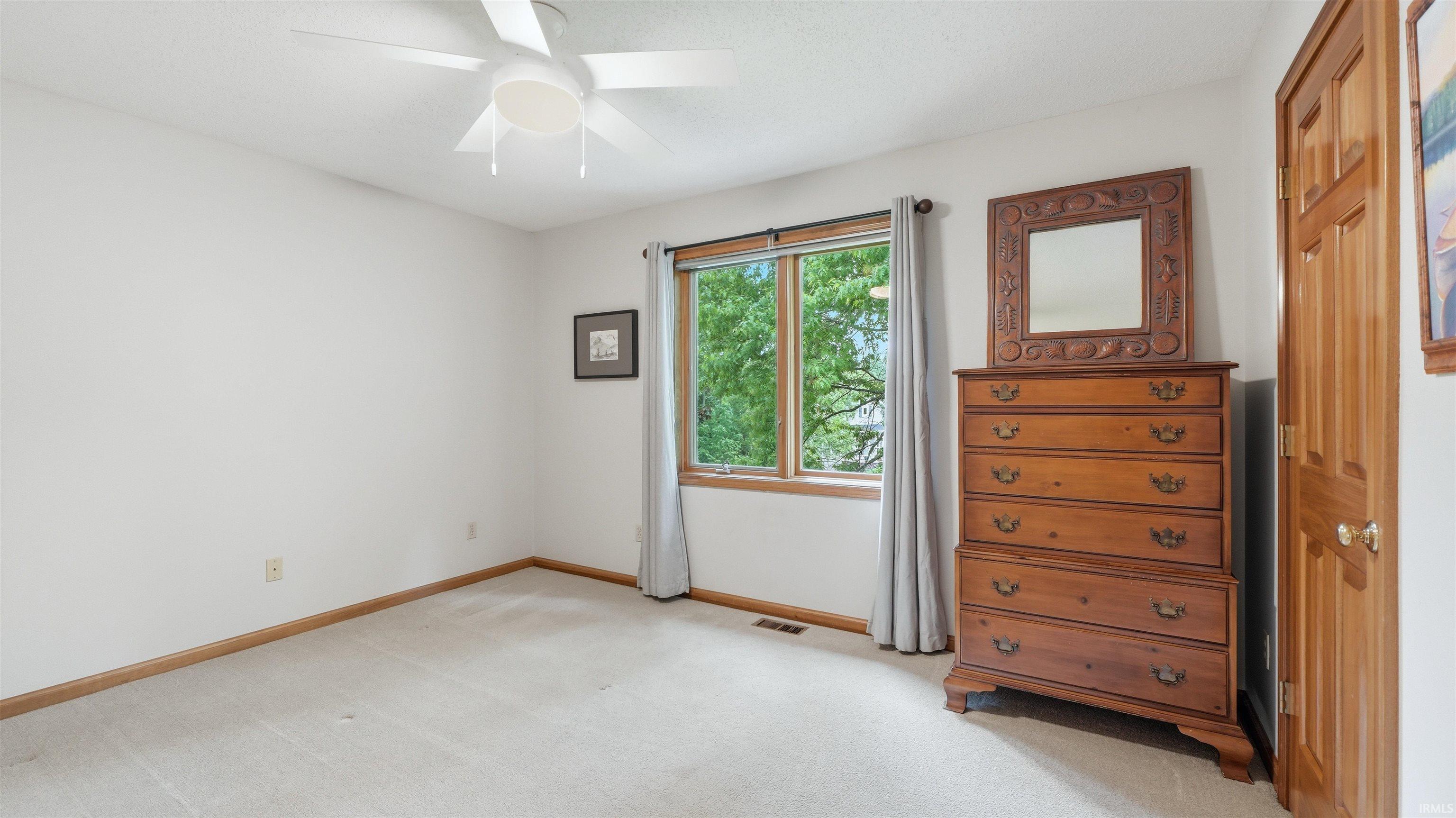 Carpeted room featuring a ceiling fan, a window with wood trim, and a paneled wood door