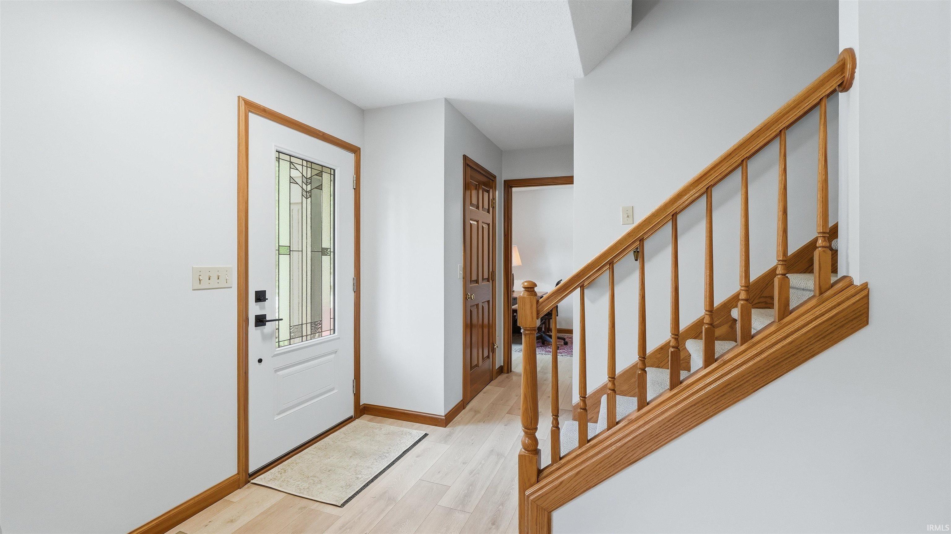 Entry foyer featuring wood-finish flooring, a white front door with leaded glass insert, and natural wood trim throughout
