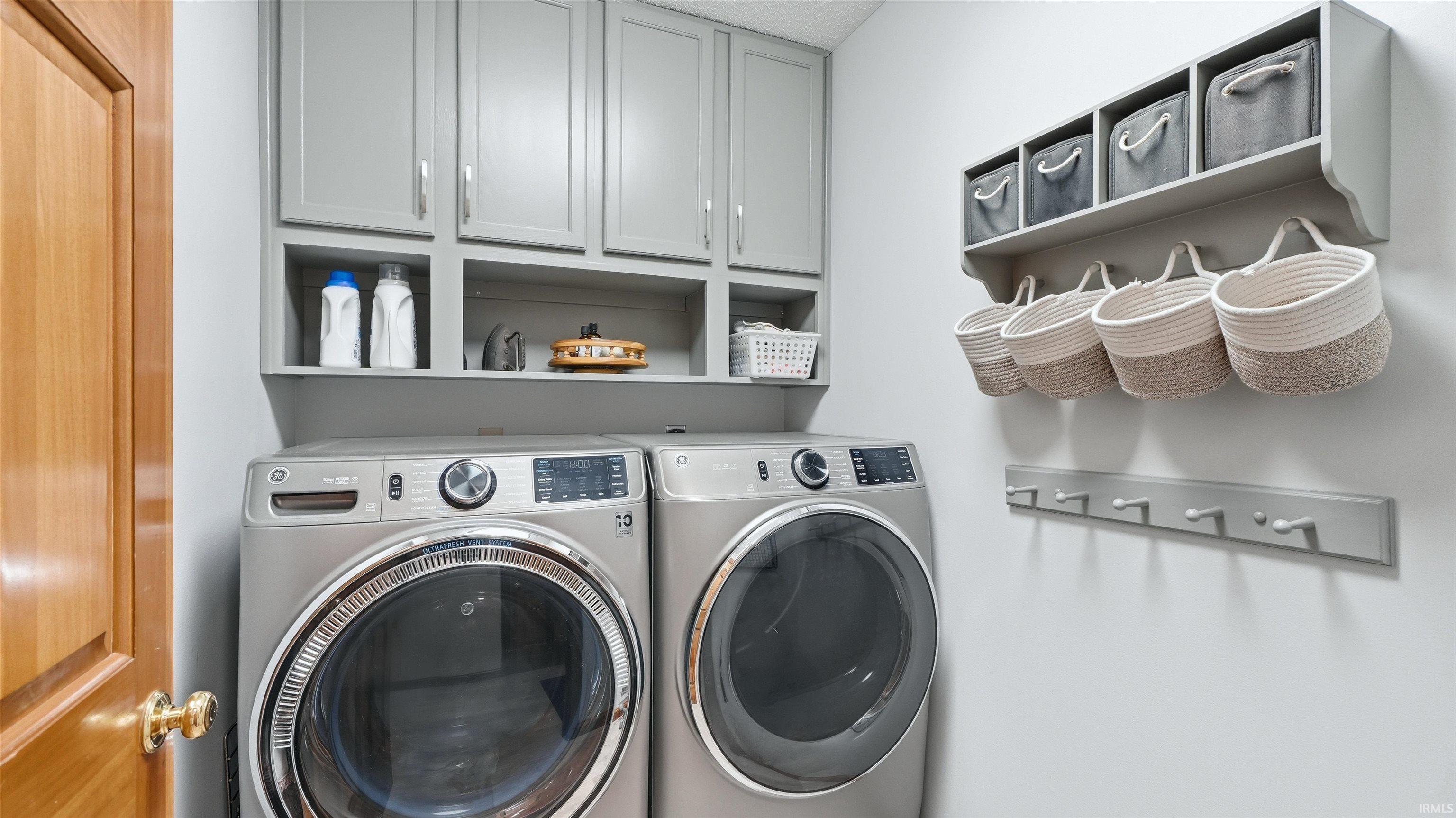 Dedicated laundry space featuring a side-by-side washer and dryer, upper cabinetry with brushed nickel hardware, and an integrated shelf