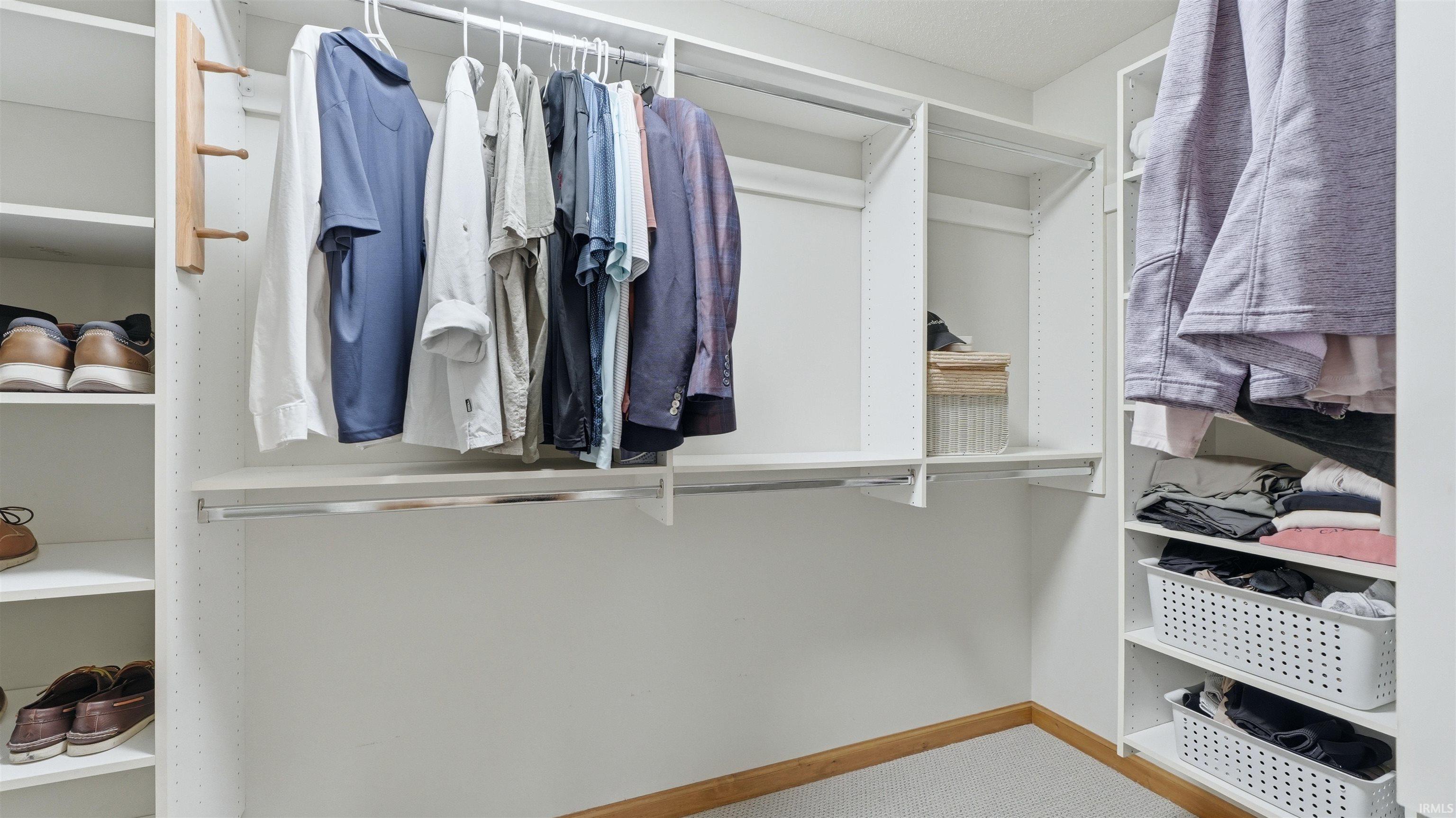 Custom closet system featuring white shelving, multiple hanging rods, dedicated shoe storage, and integrated shelving units