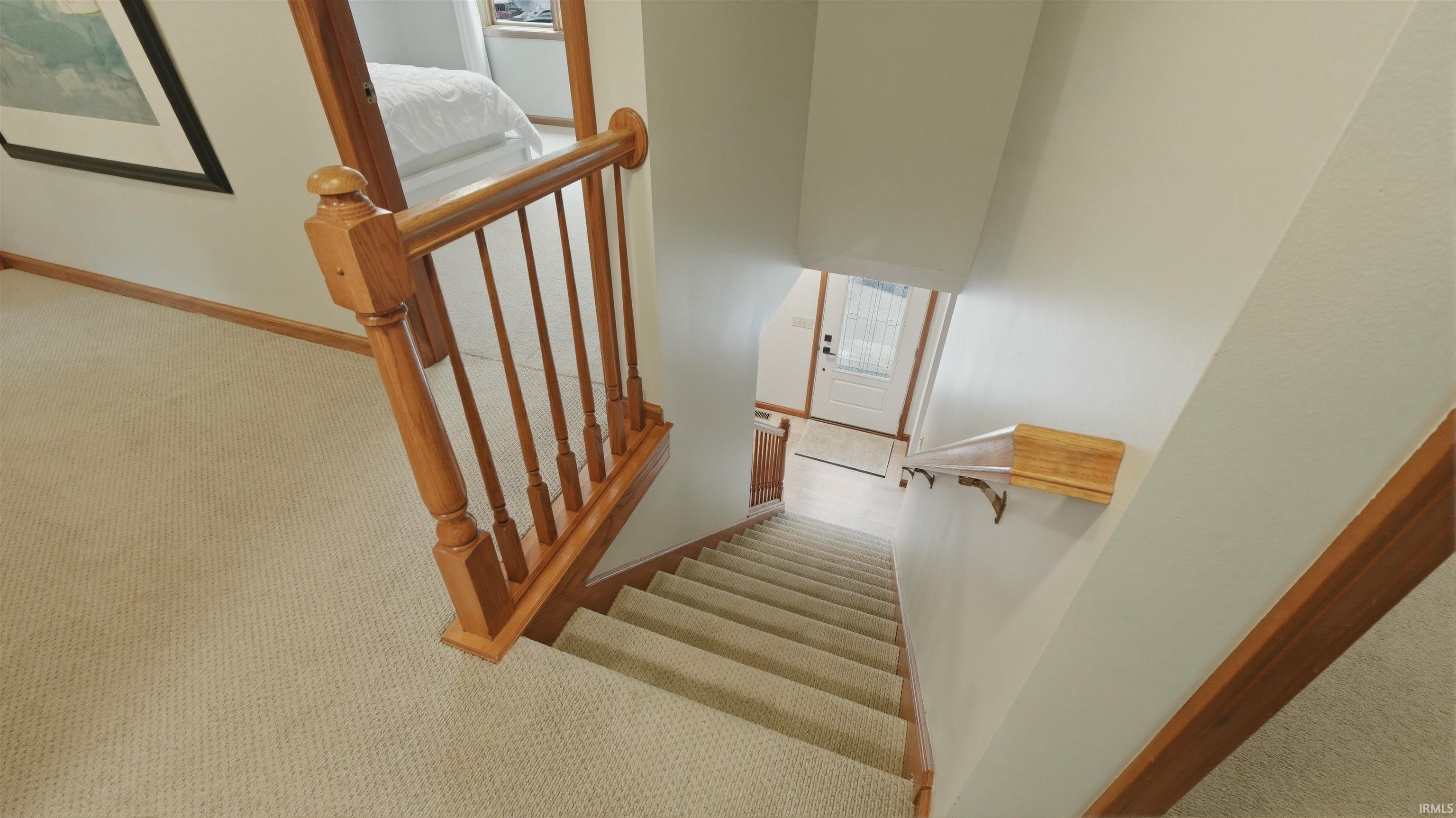 Carpeted stairway with light wood banister and handrail