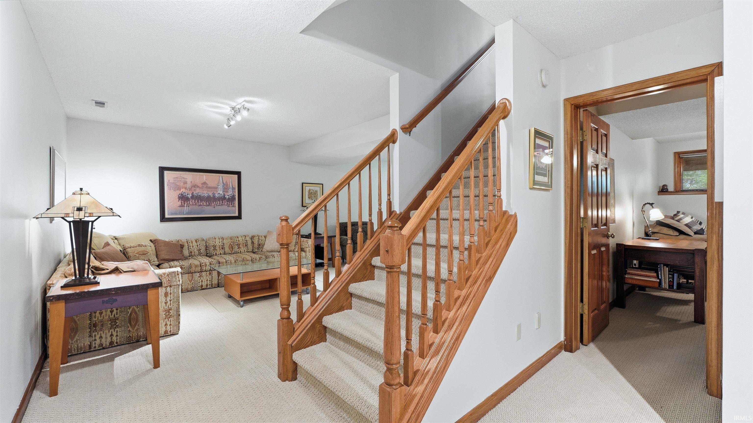 Carpeted stairway with natural wood banister, white walls, and track lighting
