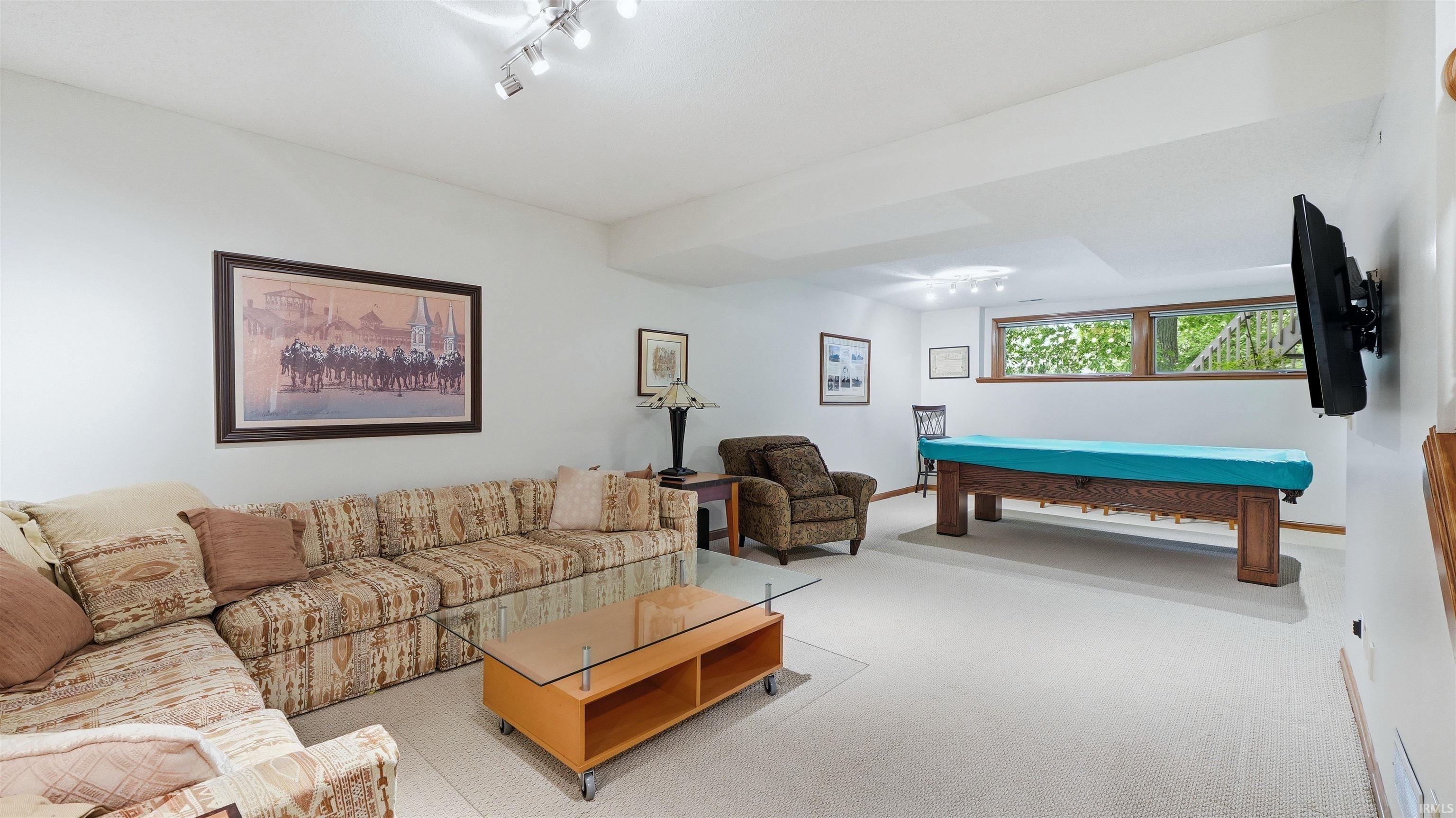 Expansive recreation room featuring light-toned carpeting, recessed lighting, and a large window with exterior greenery