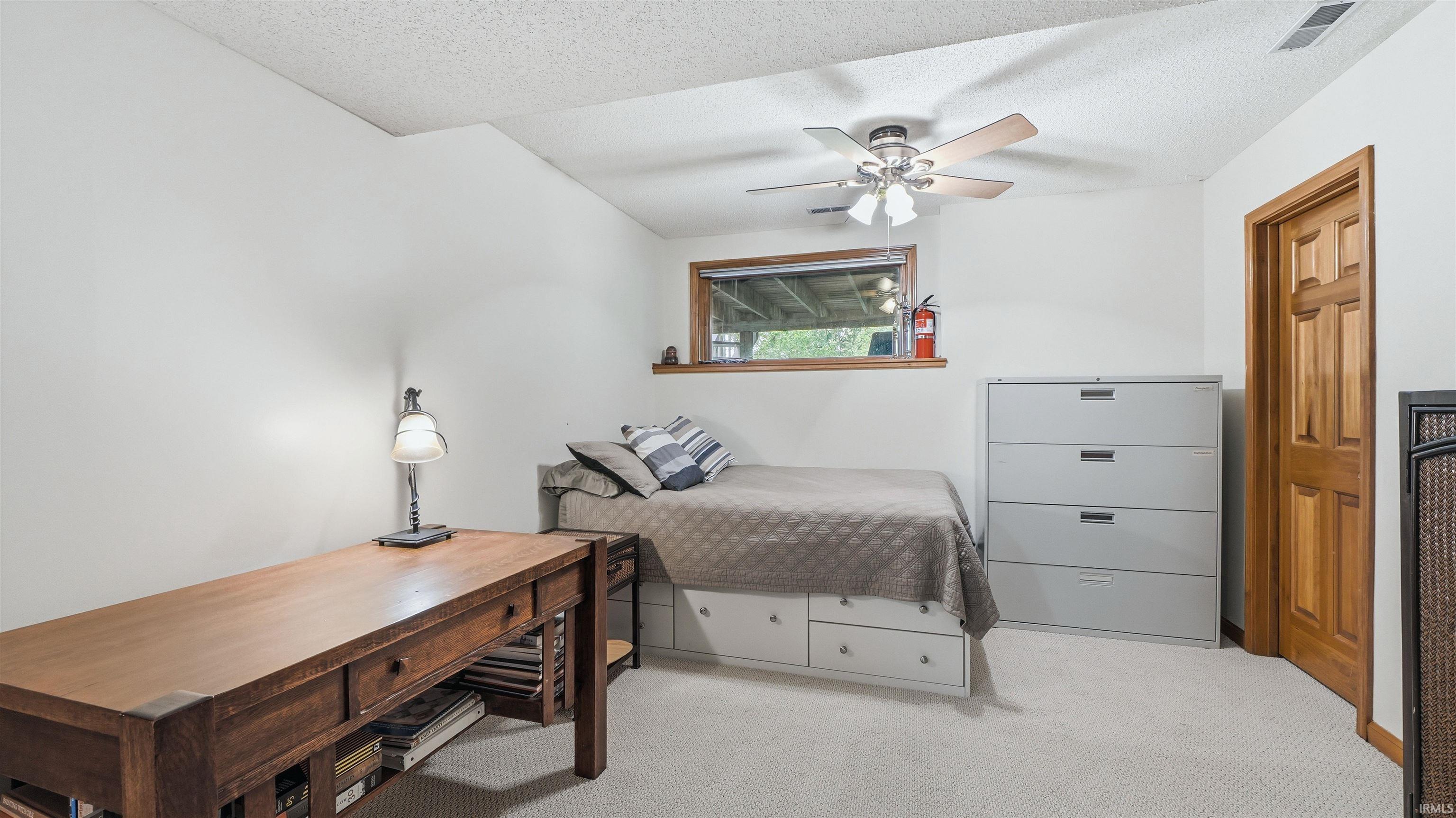Carpeted room featuring a window with wood trim, a built-in bed frame with storage drawers, a wooden door, and a ceiling fan