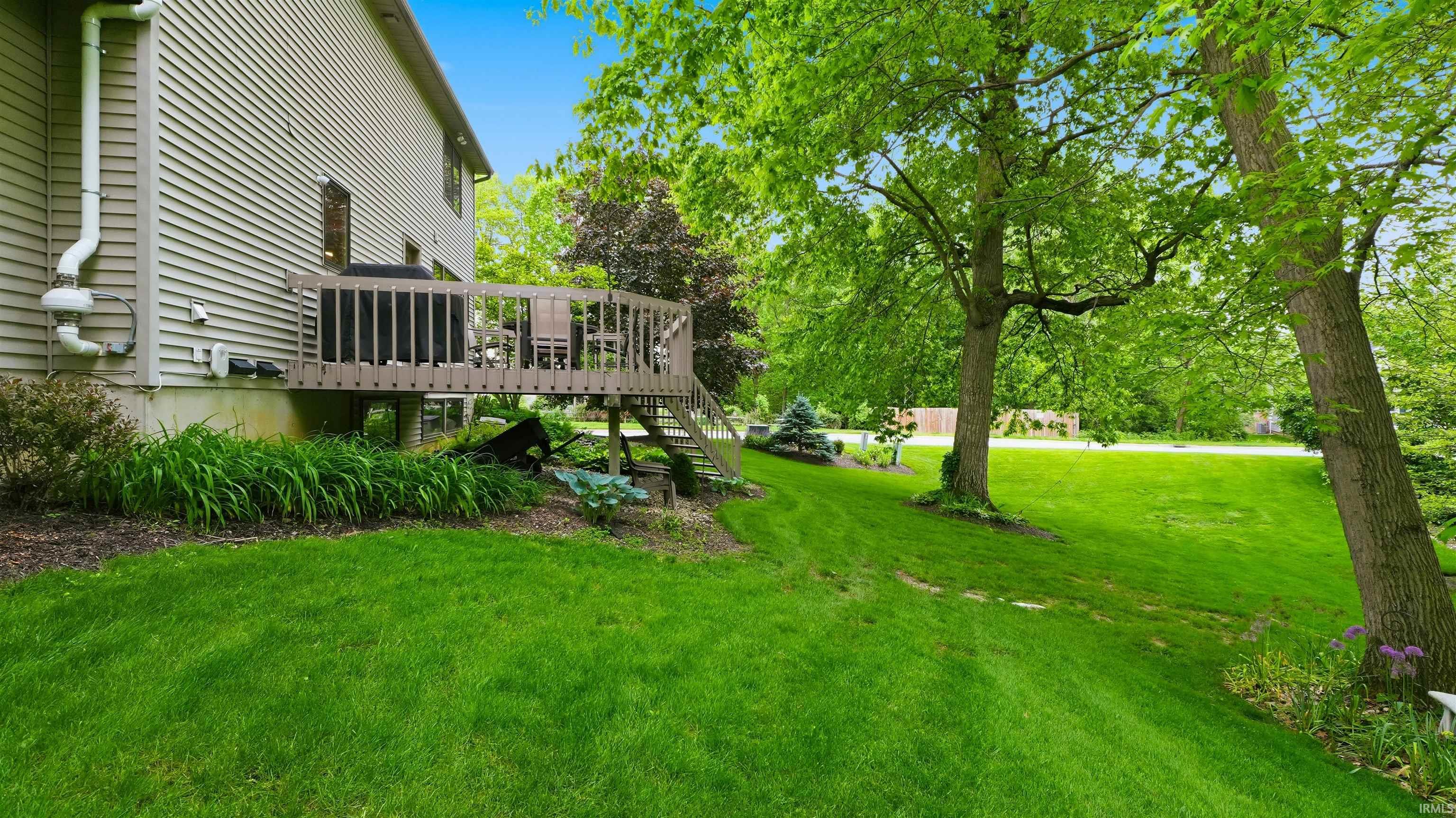 Expansive green lawn with mature trees and a multi-level wood deck