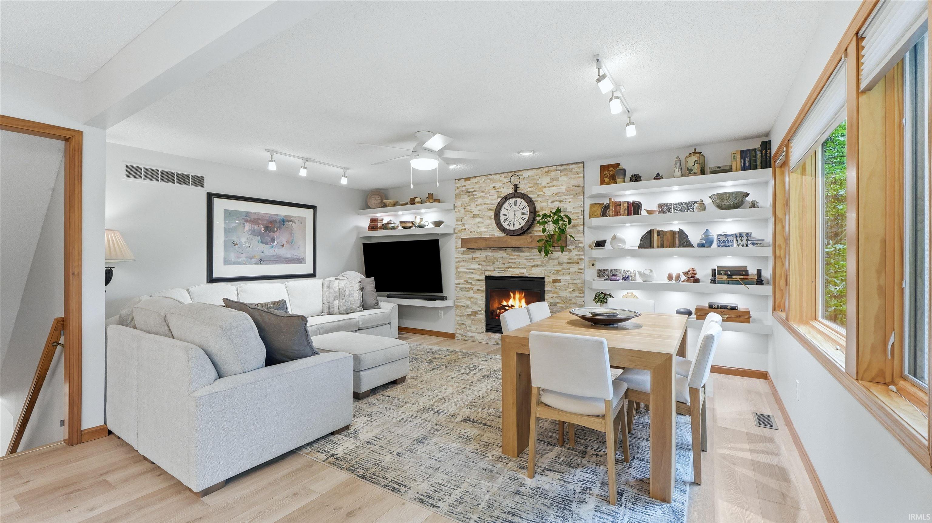 Open-concept living space featuring wood-finish flooring, a stone-clad fireplace with a wood mantle, recessed lighting, and built-in shelving with integrated illumination