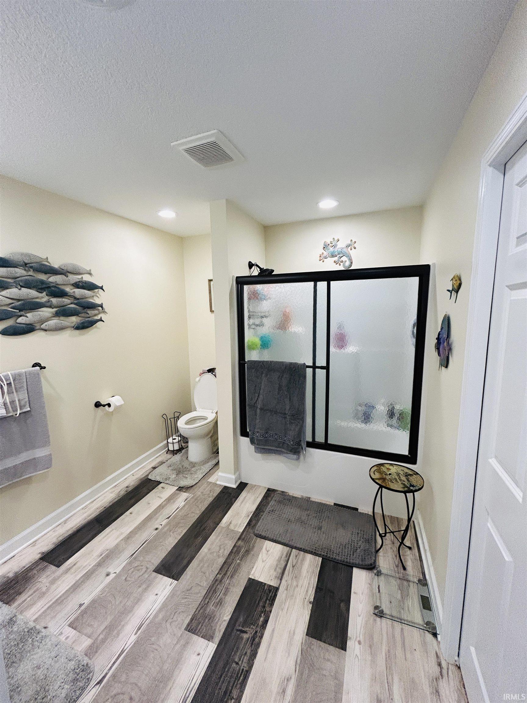 Bathroom featuring multi-tone wood-finish flooring, recessed lighting, and a shower with black framed sliding glass doors