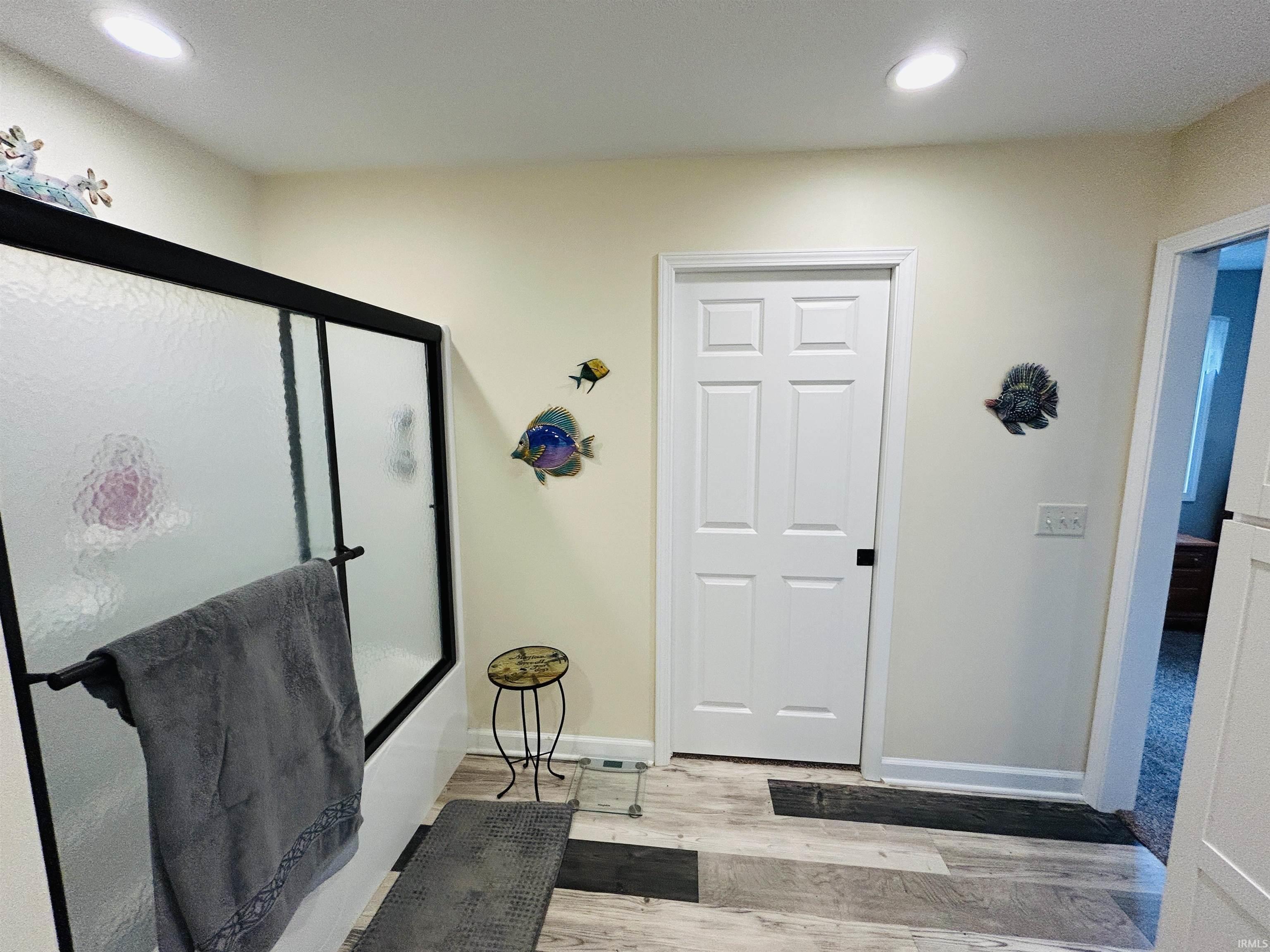 Walk-in shower featuring a sliding frosted glass door with black framing, recessed ceiling lighting, and wood-finish flooring